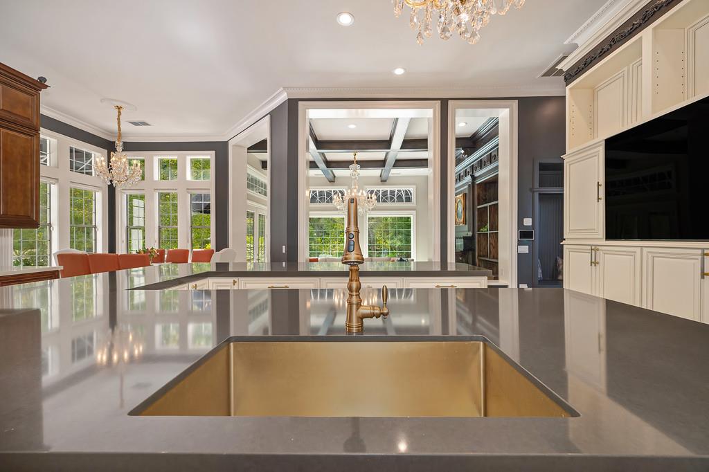 Kitchen with a large stone island, brass sink, white cabinetry, and tall windows overlooking the dining area.