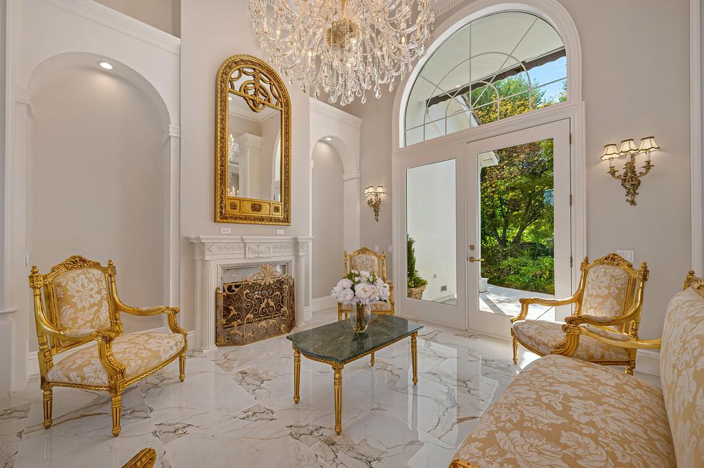 Formal living room with a marble fireplace, crystal chandelier, and arched glass entry.