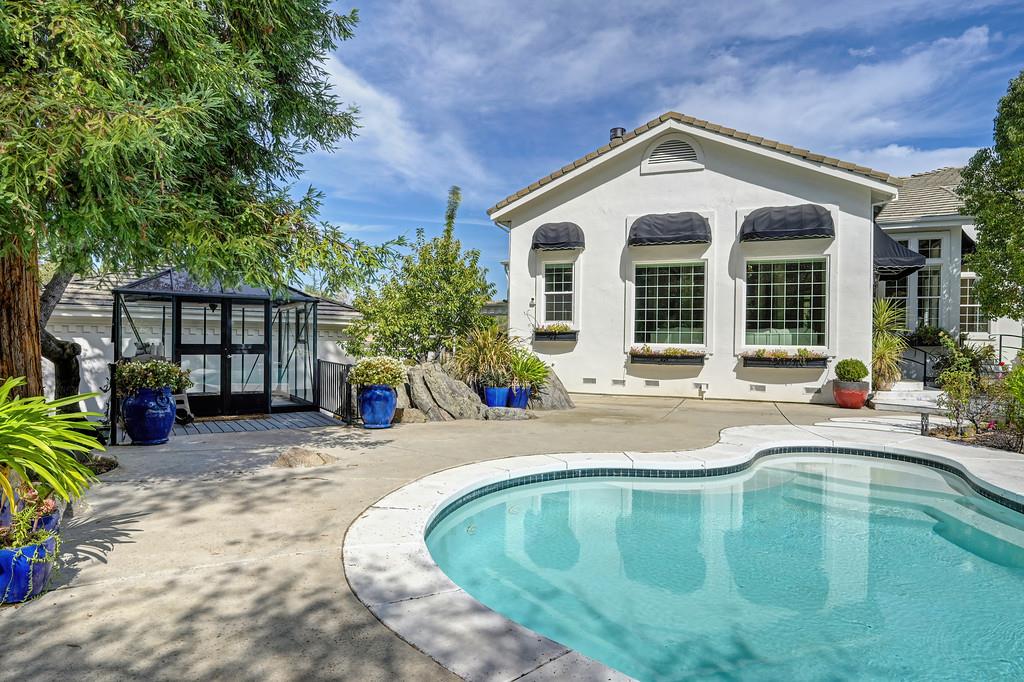 Backyard pool beside a white stucco home, with a glass-enclosed structure and landscaped patio.