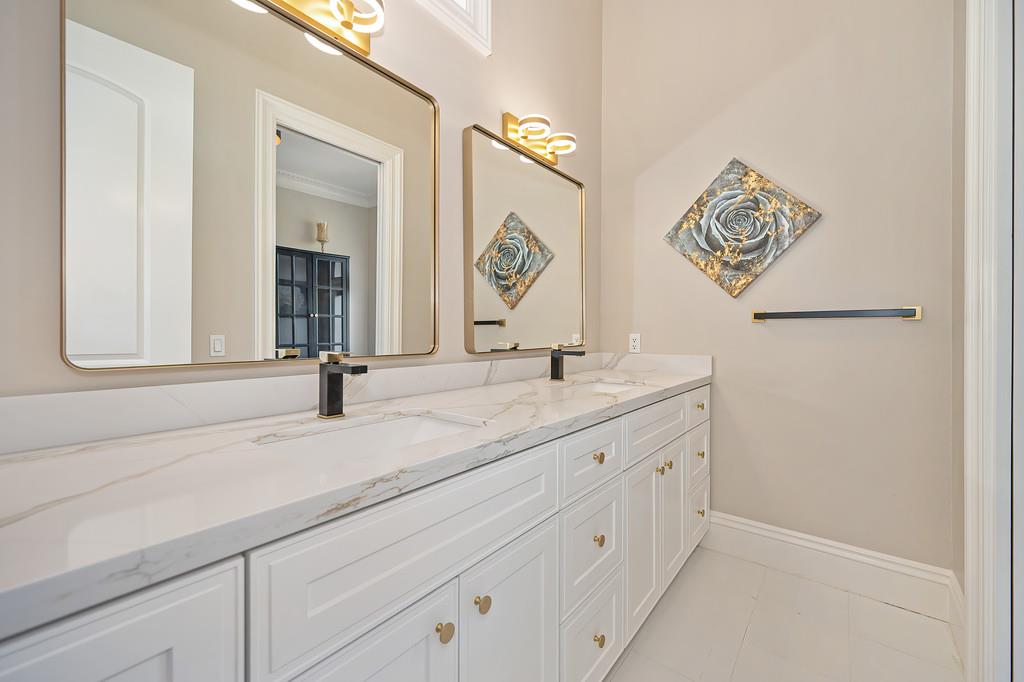 Bathroom with a long double vanity, marble-look countertop, brass fixtures, and framed mirrors.