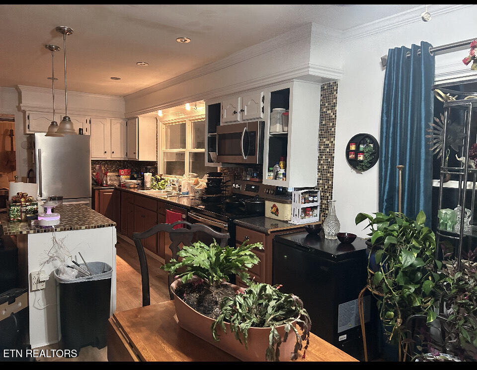 Kitchen with dark wood cabinets, stainless-steel refrigerator, mosaic tile accents, and plants on the table.