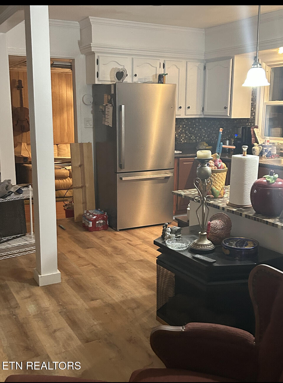 Kitchen with stainless steel refrigerator, white cabinets, and dark mosaic tile backsplash.