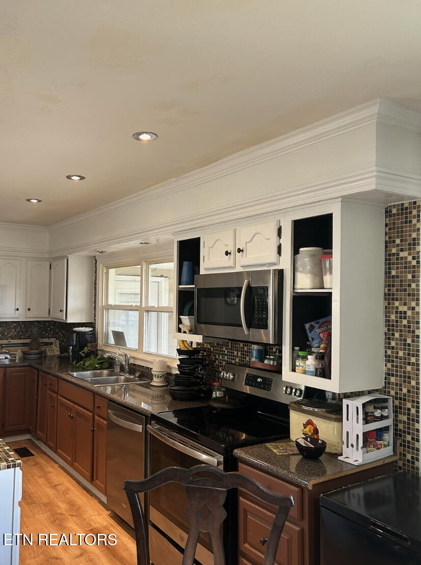 Kitchen with white upper cabinets, reddish-brown lower cabinets, and a multicolored tile backsplash.
