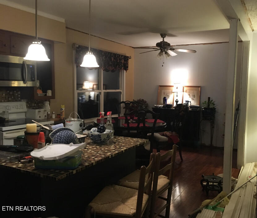 Kitchen and dining area with a tiled peninsula, crowded countertop, and dark wood flooring.
