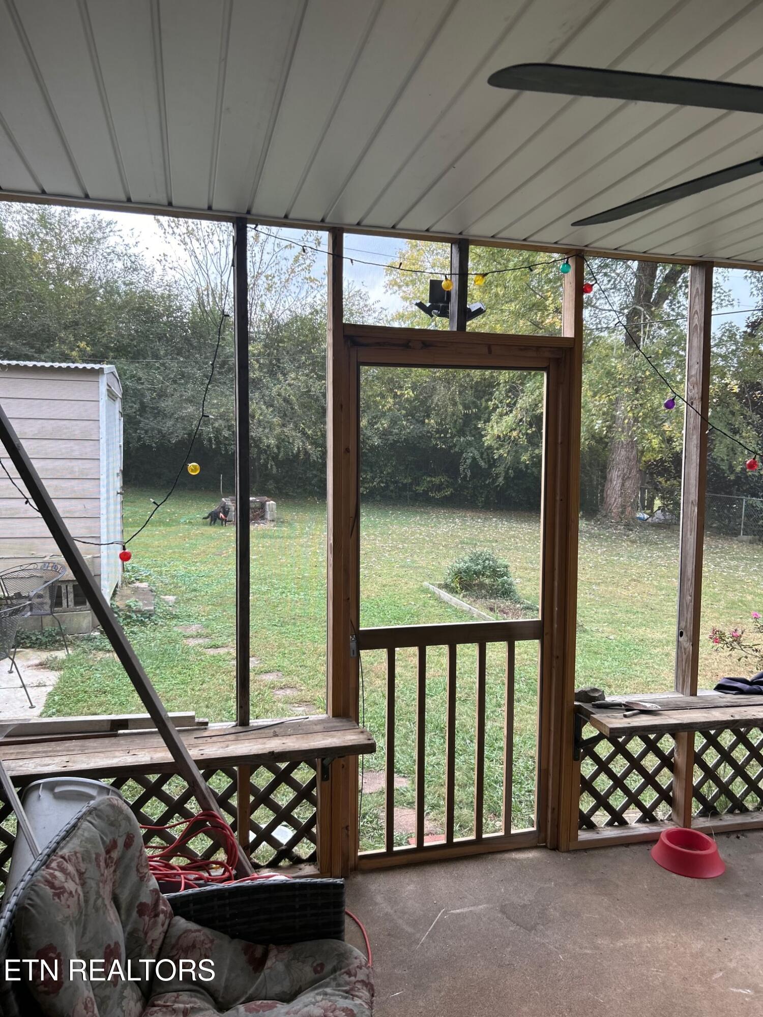 Covered back porch with wooden railings and string lights overlooking a grassy, tree-lined backyard.