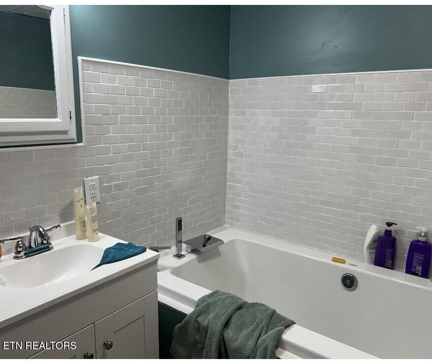 Bathroom with white bathtub, vanity, gray tile walls, and teal upper walls.