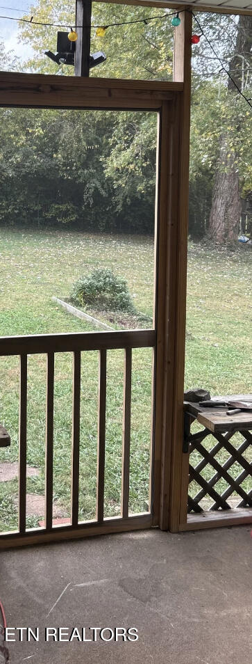 Screened porch with wooden framing and railing overlooking a grassy, tree-lined yard.