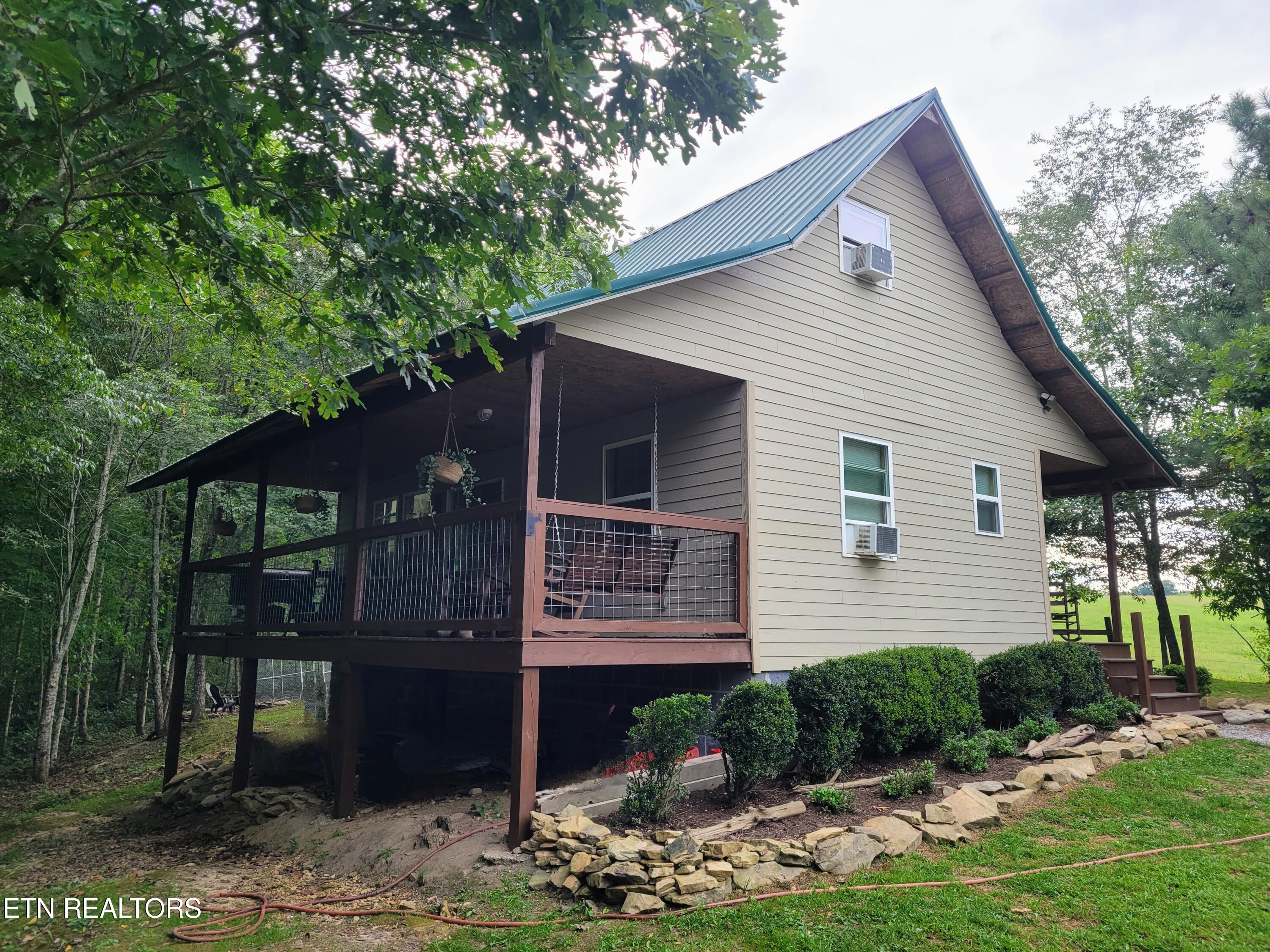 Raised beige home with a teal metal roof and covered porch among trees.