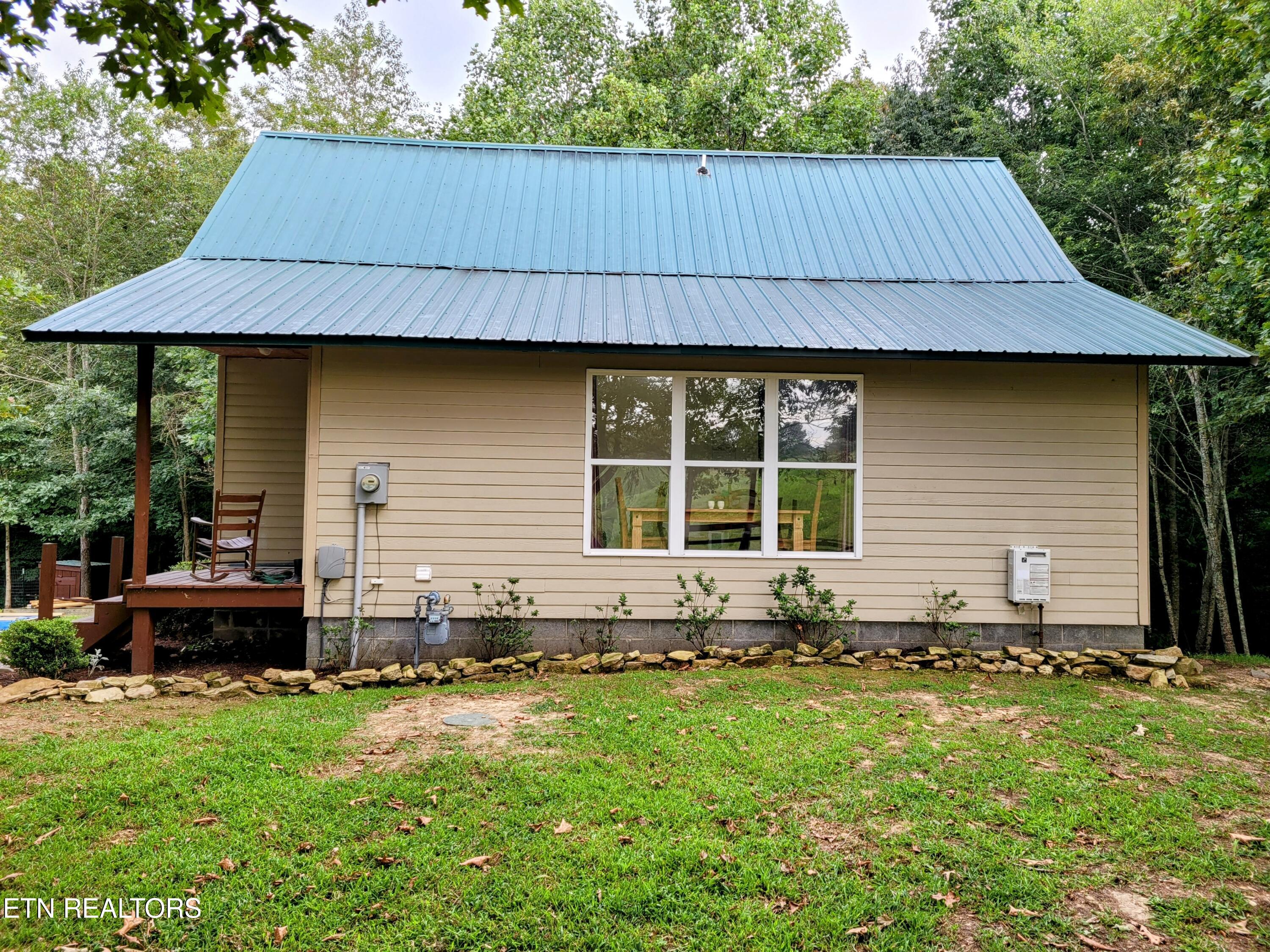 Beige-sided home with a broad metal roof, covered deck, and wooded surroundings.