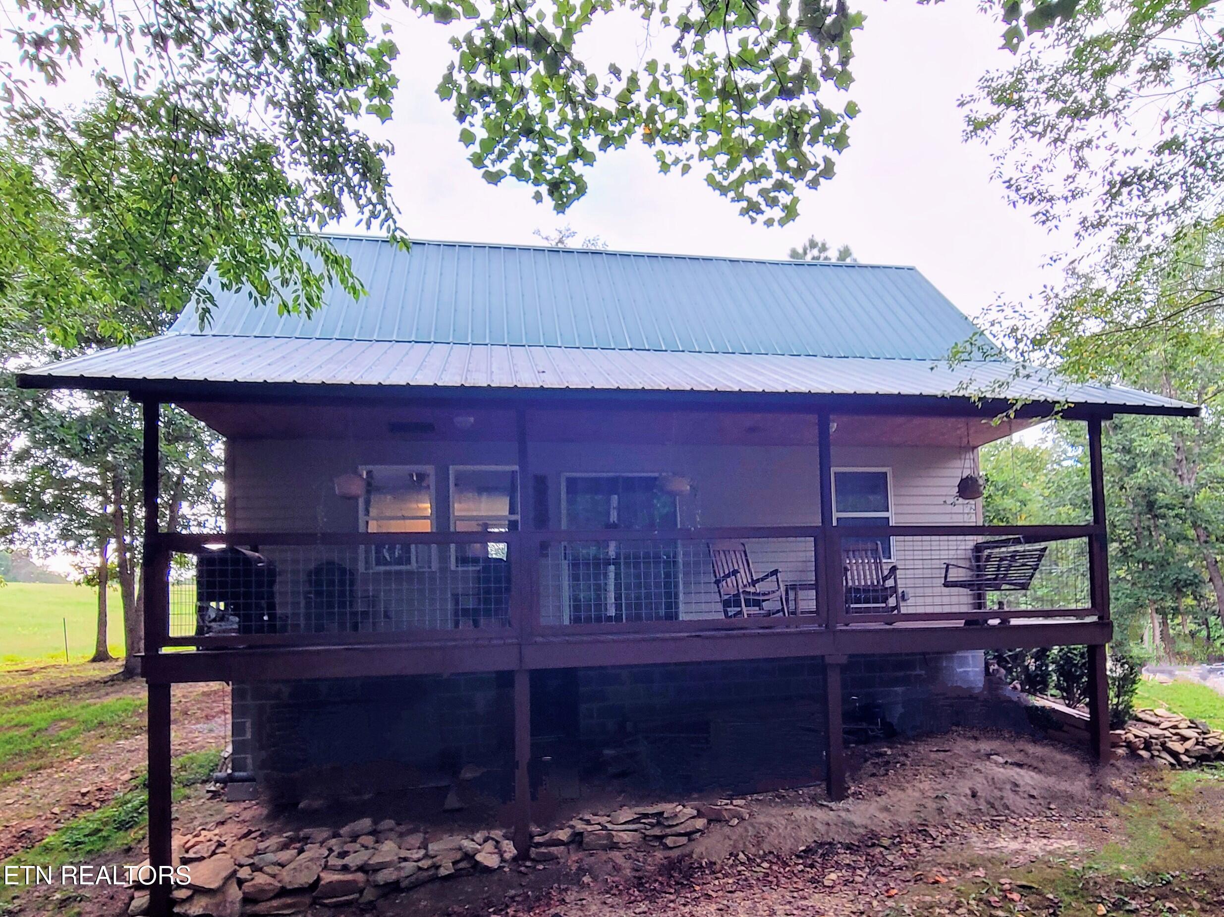 Raised house with a metal roof and a spacious screened porch furnished with rocking chairs and a swing.