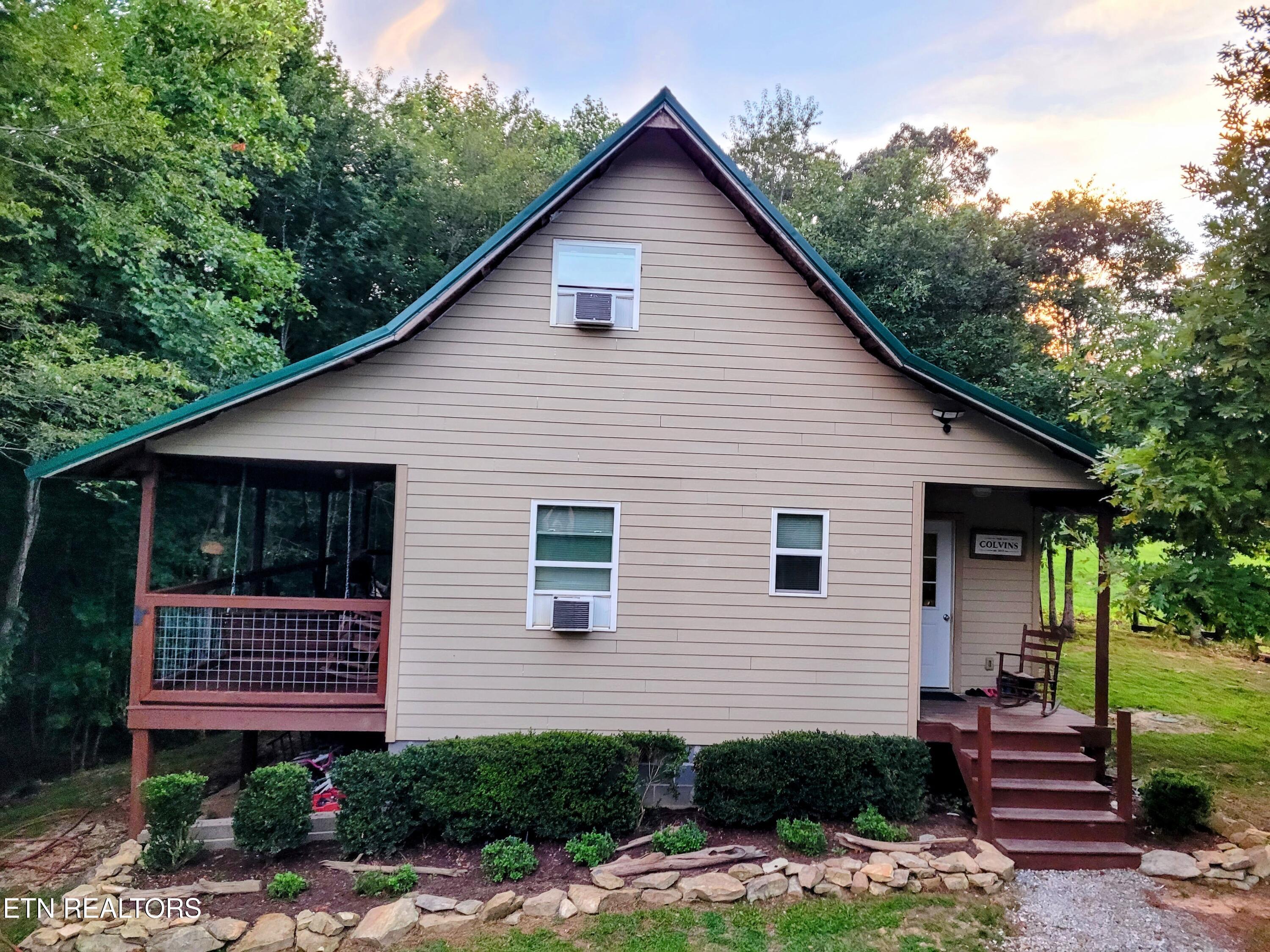 Home with a steep green-trimmed gable, screened porch, and covered entry amid trees.