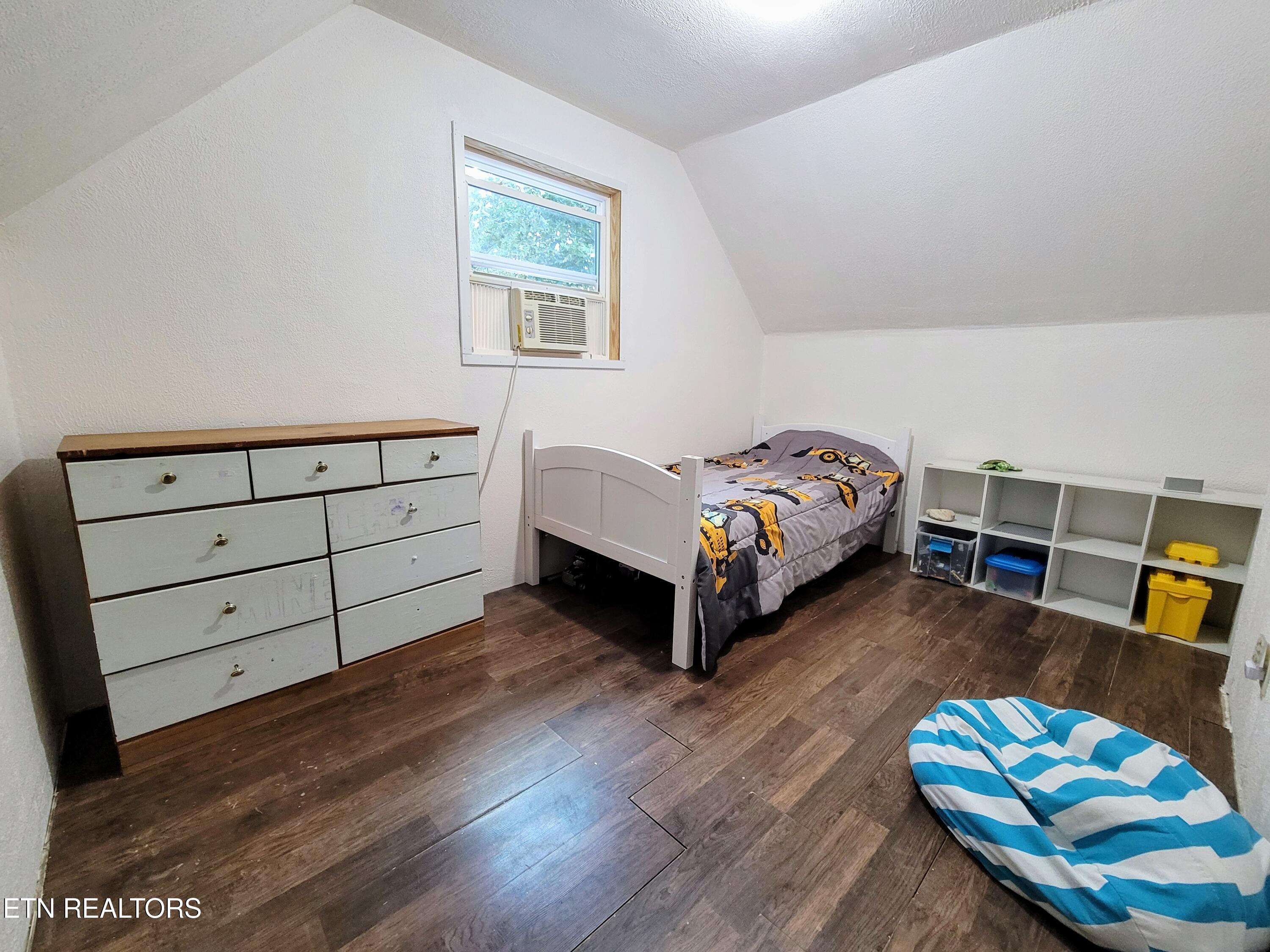 Bedroom with a single bed, construction-vehicle bedding, white dresser, and window air conditioner.