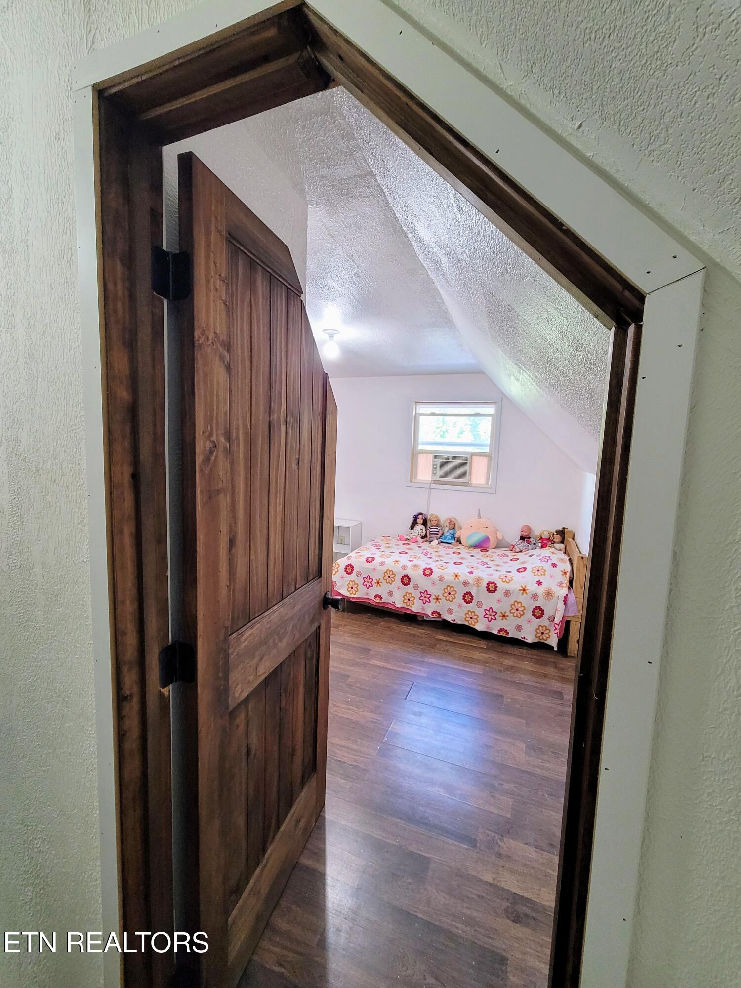 Bedroom with a sloped ceiling, wooden floor, flower-patterned bedspread, and open wooden door.