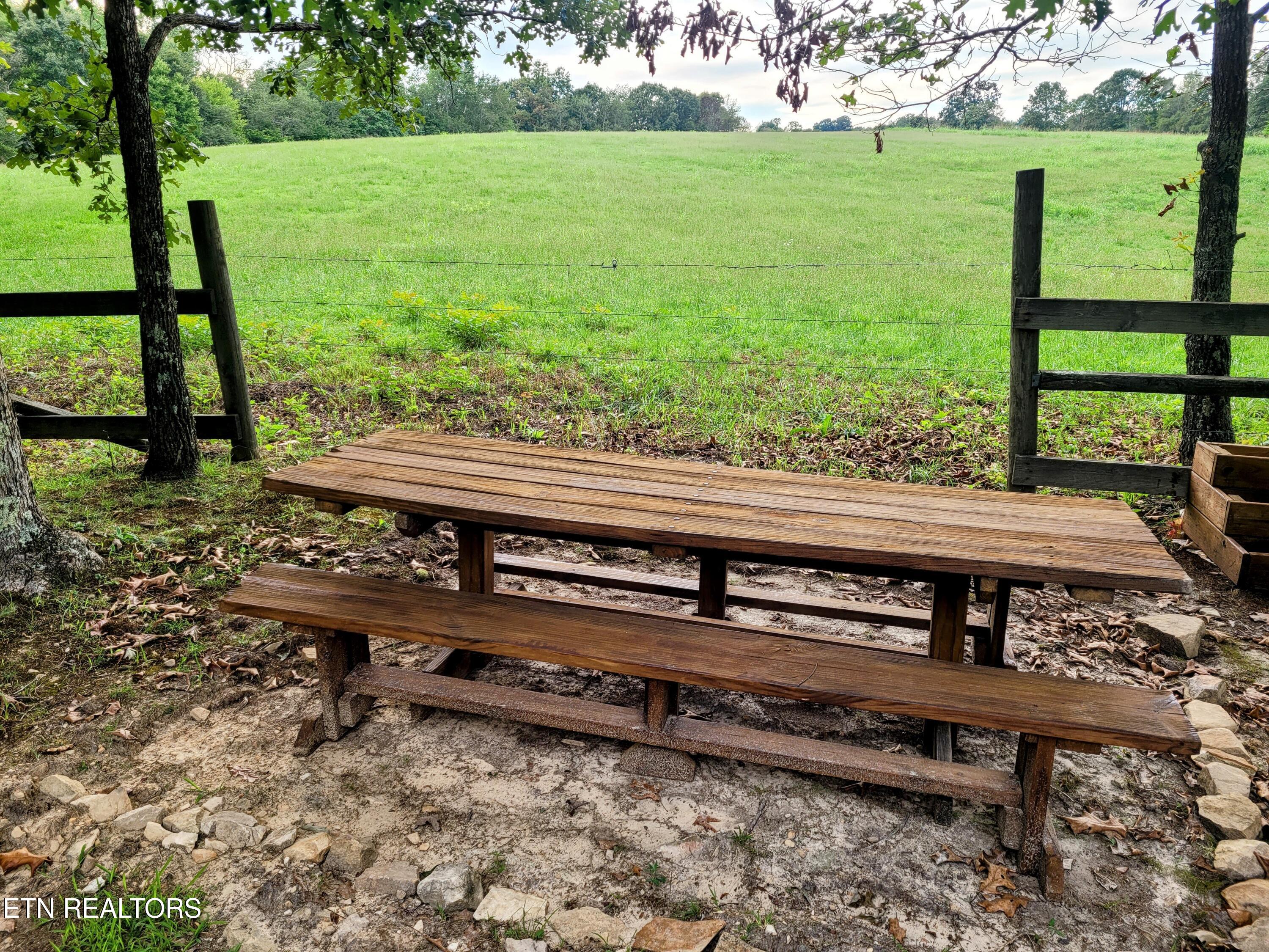 Wooden picnic table beside a fenced green pasture, shaded by trees.