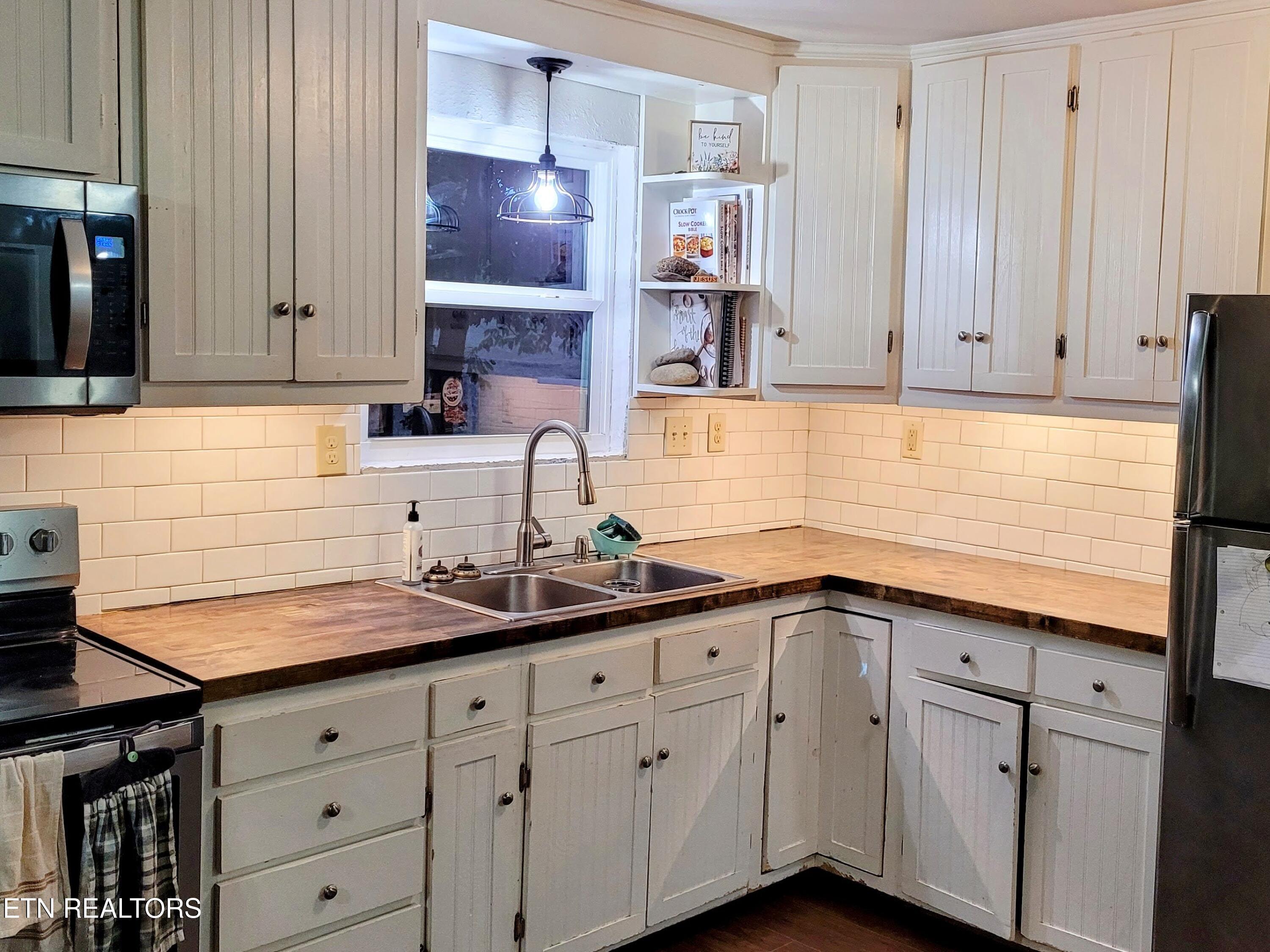 Kitchen with white paneled cabinets, wood countertops, and a stainless-steel sink beneath a window.