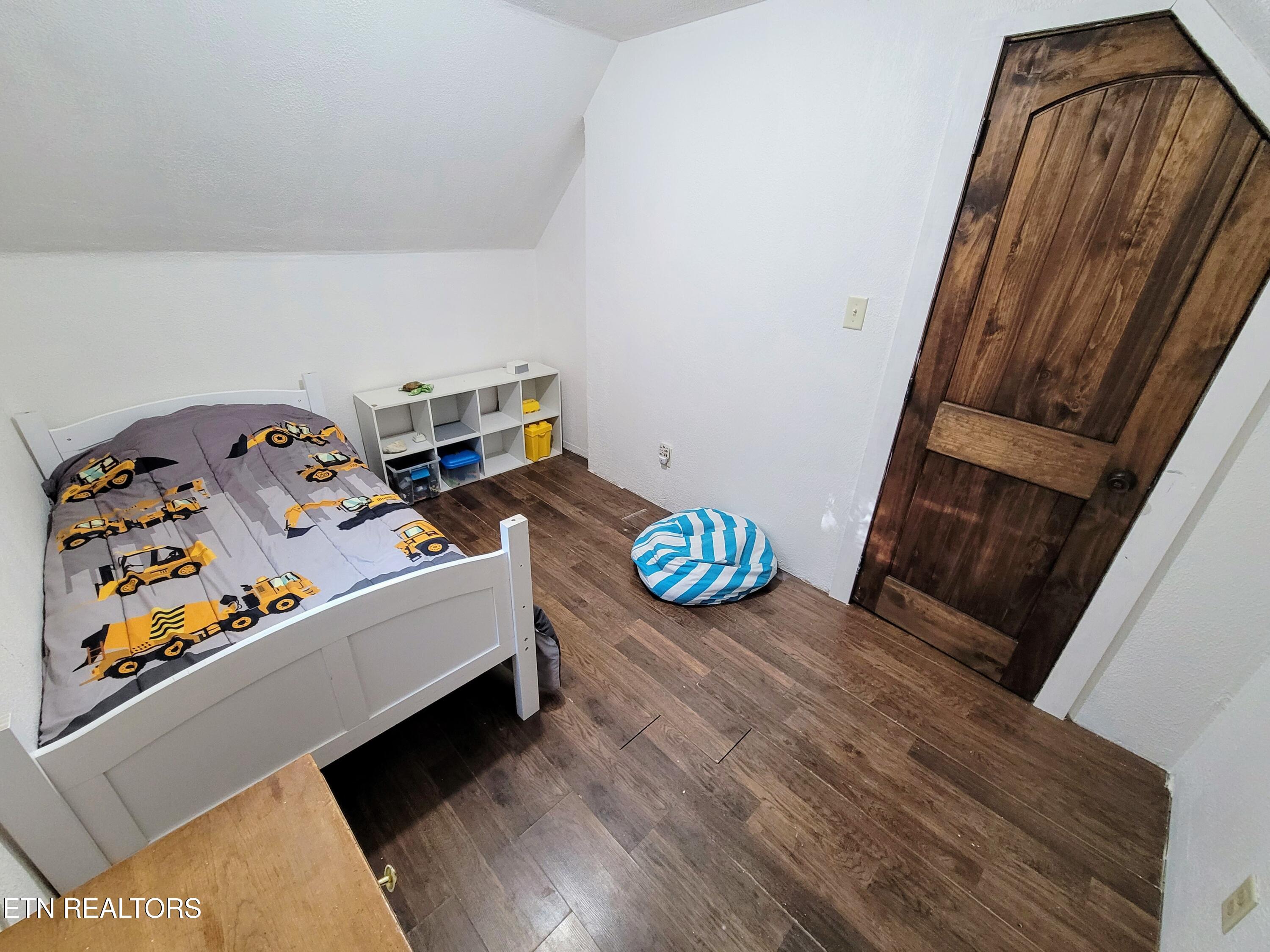 Small bedroom with construction-vehicle bedding, a white cubby shelf, and a rustic wooden door.