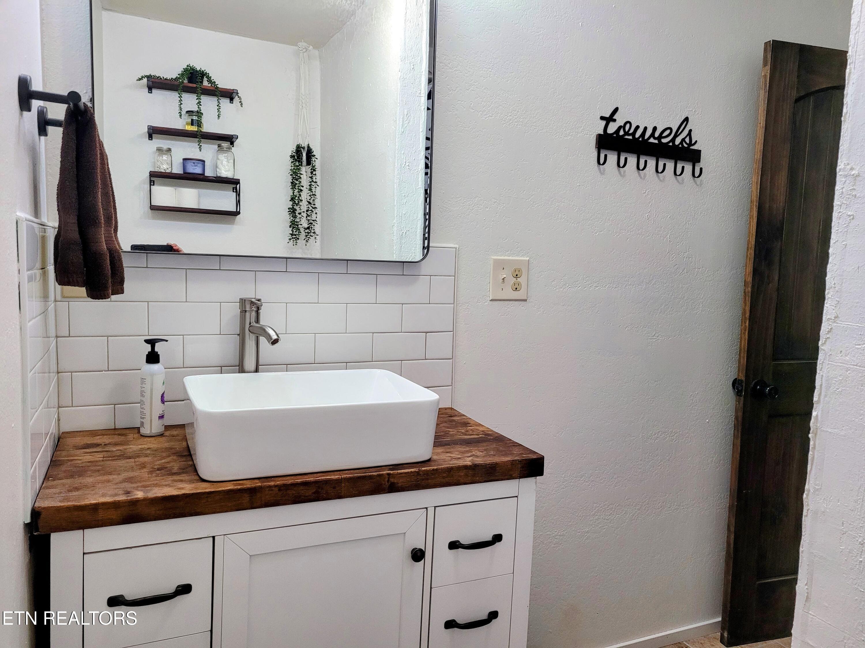 Bathroom vanity with a white vessel sink, rustic wood countertop, subway tile, and floating shelves.