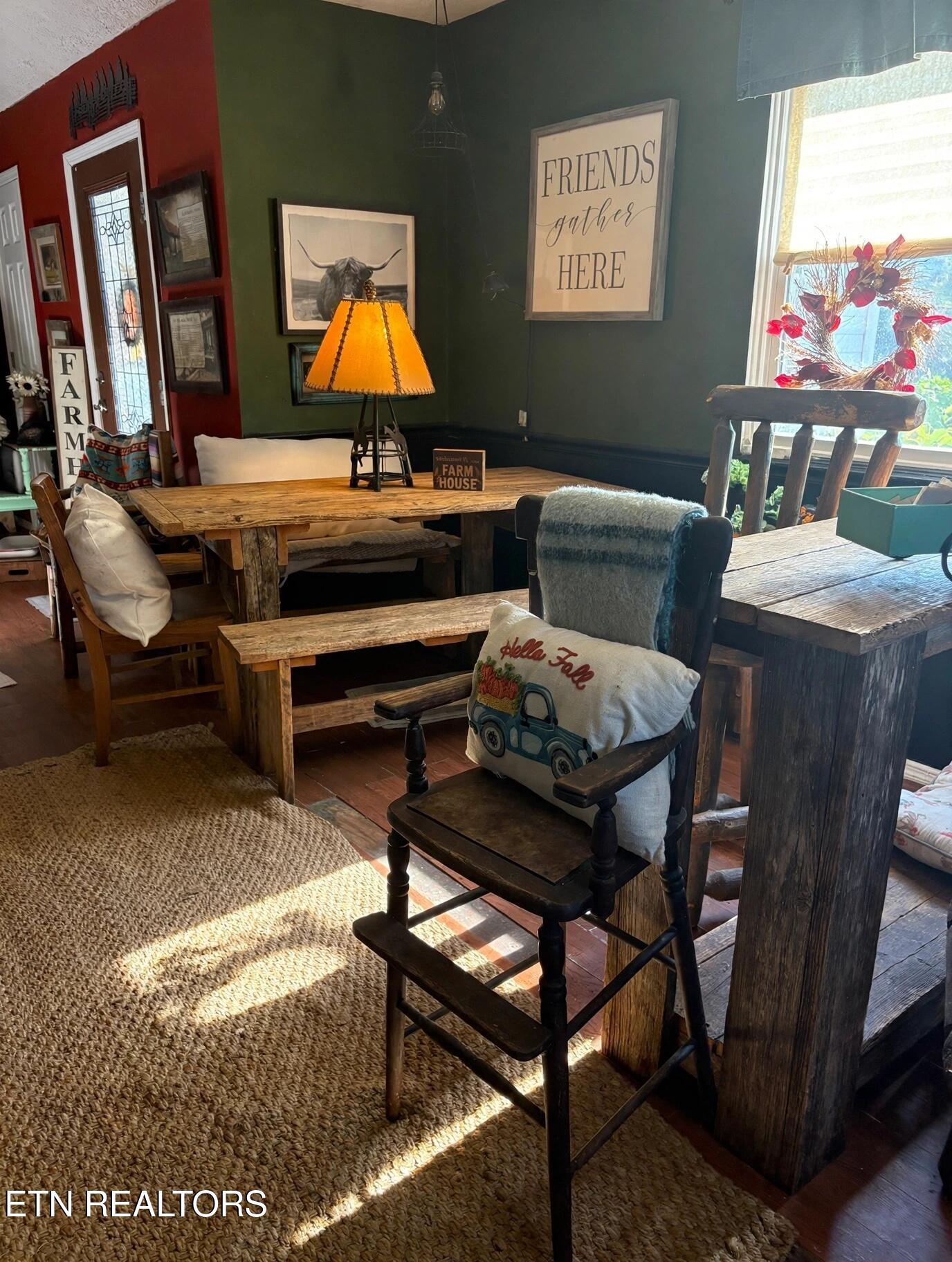 Rustic dining area with a farmhouse table, wooden benches, woven rug, and a sunny window.