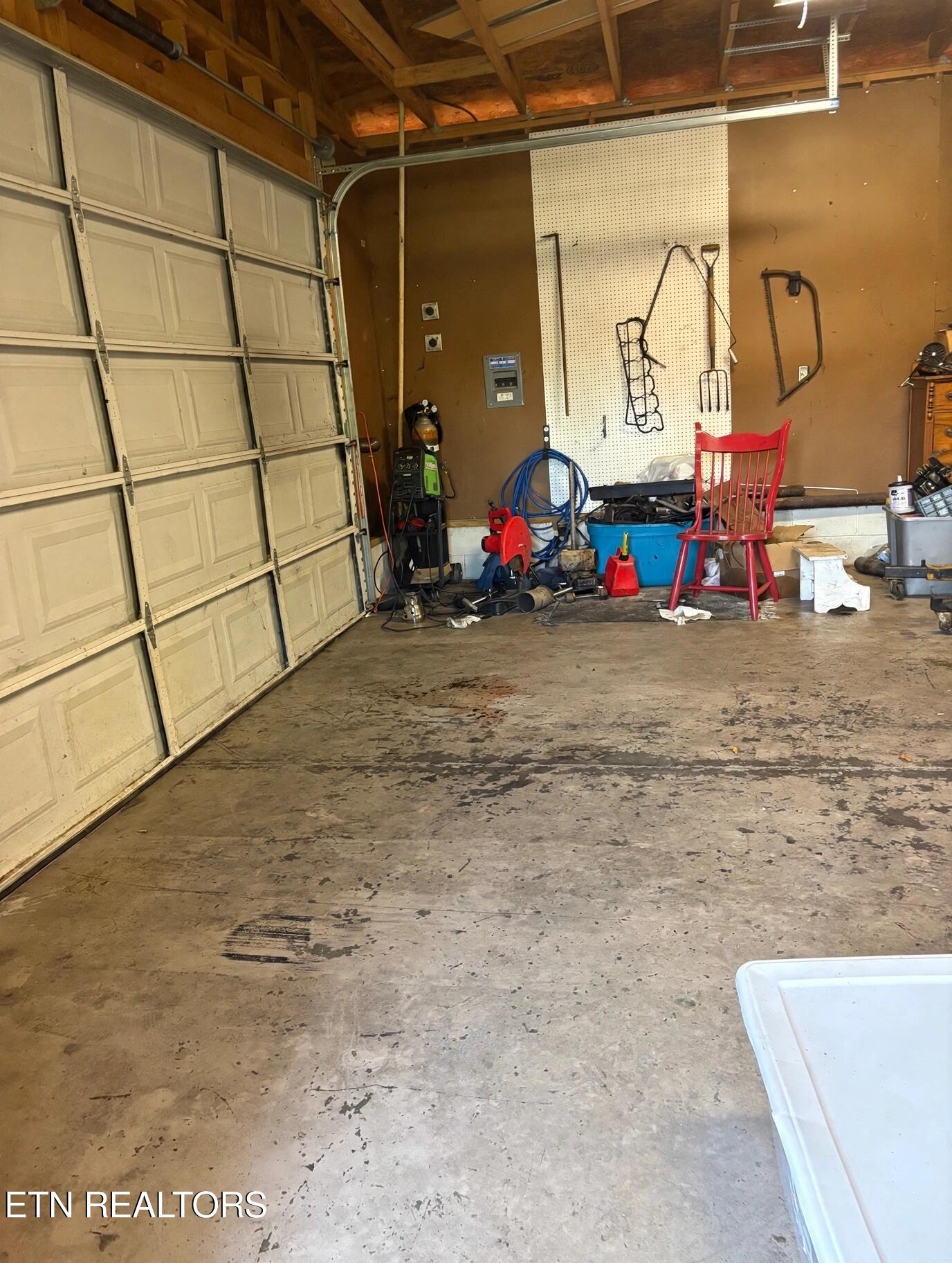 Garage interior with a large segmented door, exposed rafters, and tools along the wall.