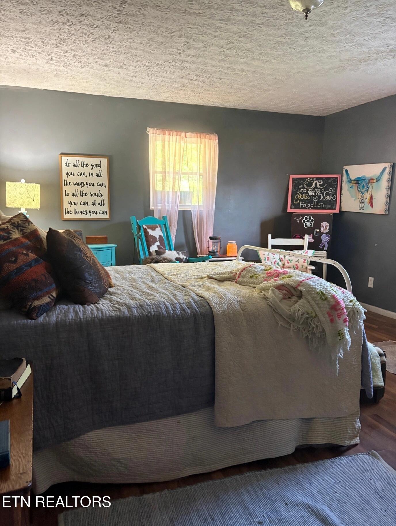 Bedroom with a large gray-quilted bed, sheer pink curtains, turquoise chair, and dark gray walls.