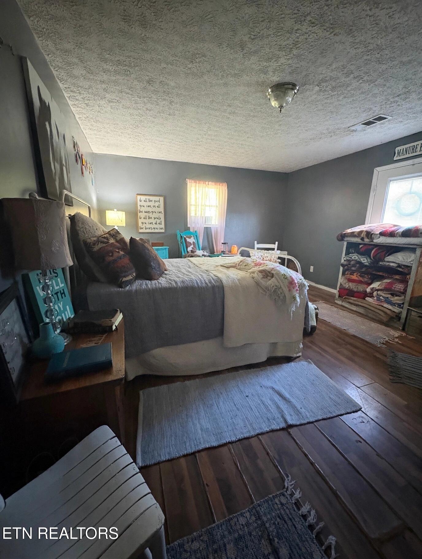 Furnished bedroom with gray bedding, a turquoise bedside table, and folded blankets on a rack.