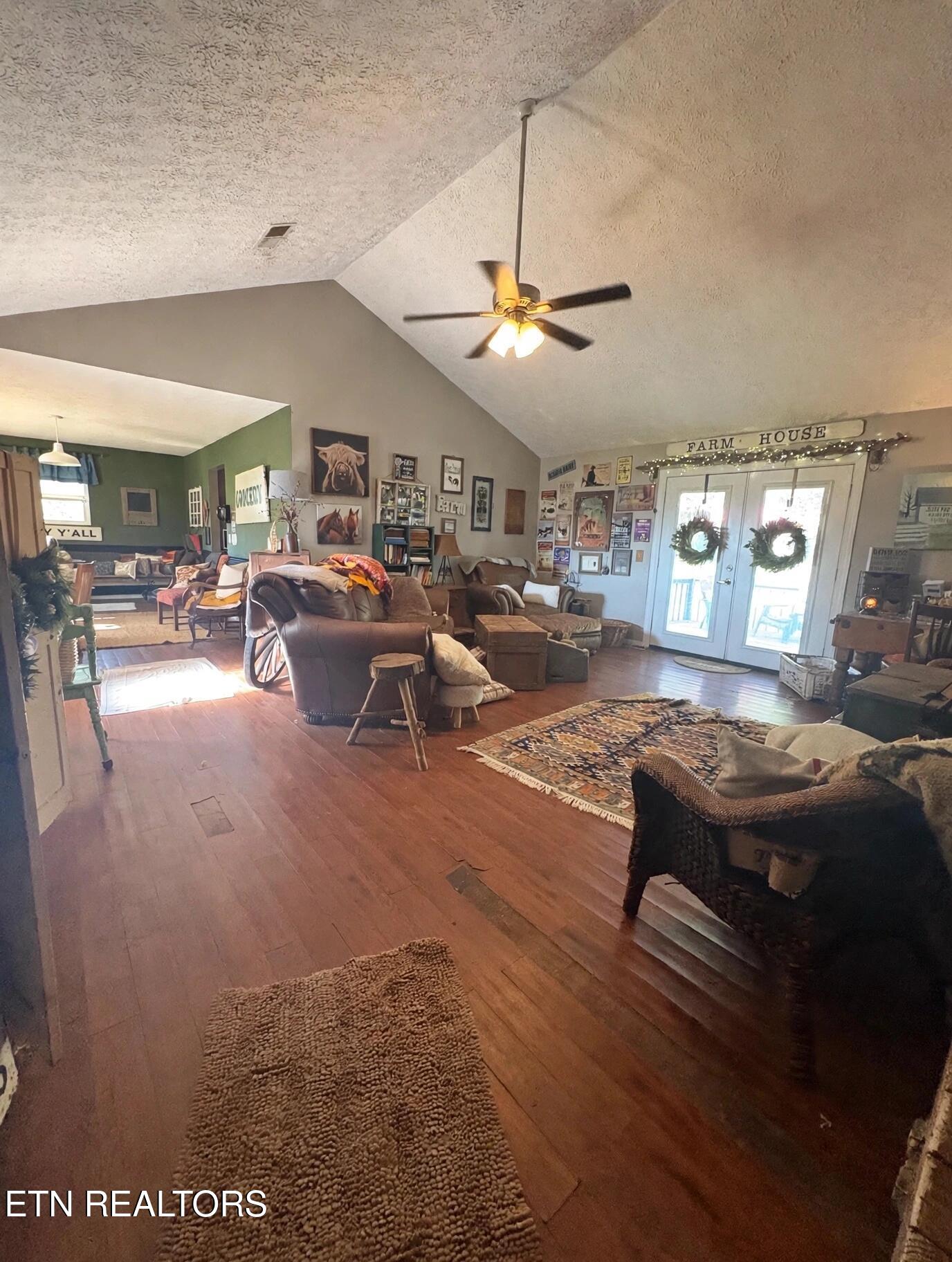 Furnished living room with vaulted ceiling, ceiling fan, hardwood floors, and wreaths on glass-panel doors.