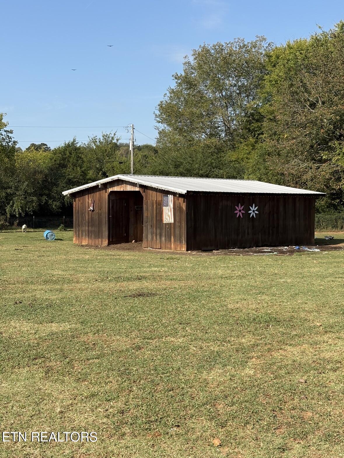 Wooden outbuilding with a metal roof in a grassy yard, decorated with flowers and an American flag.