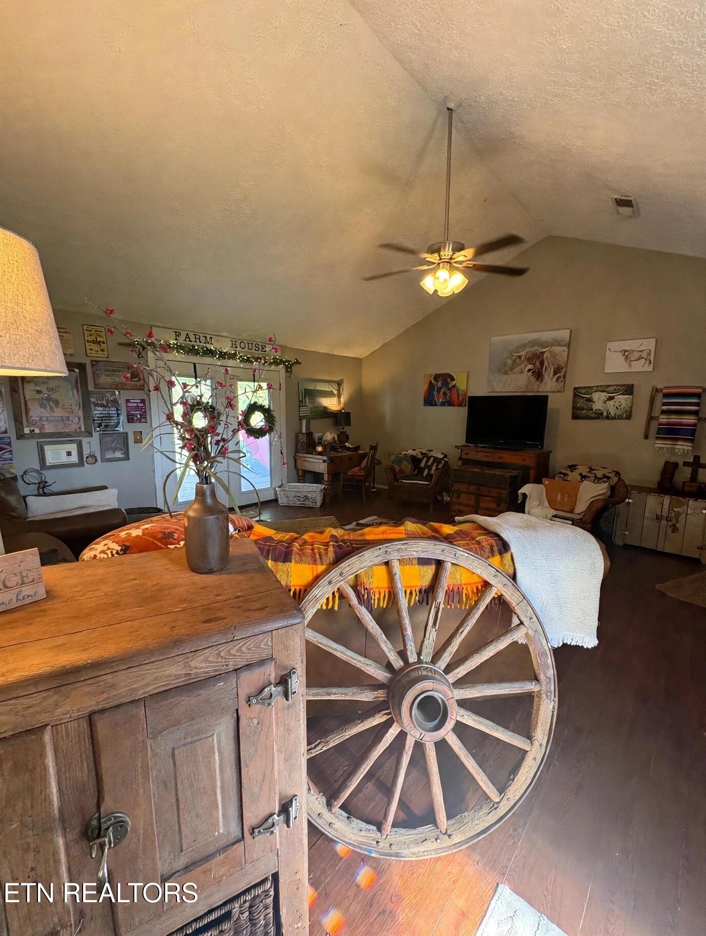 Farmhouse-style living room with vaulted ceiling, wagon-wheel table, rustic chest, and colorful throw.