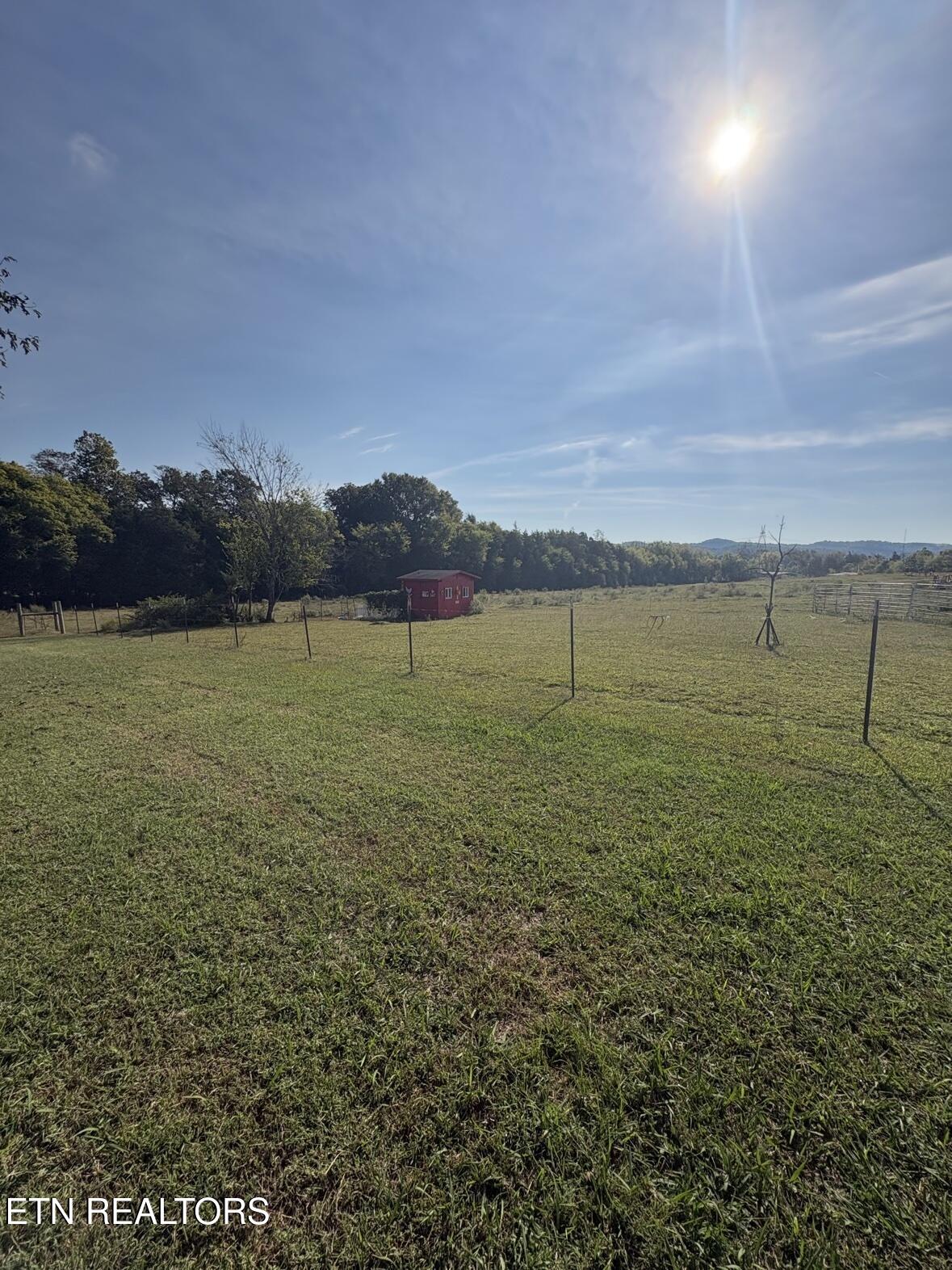 Fenced rural pasture with a small red outbuilding and wooded hills in the distance.