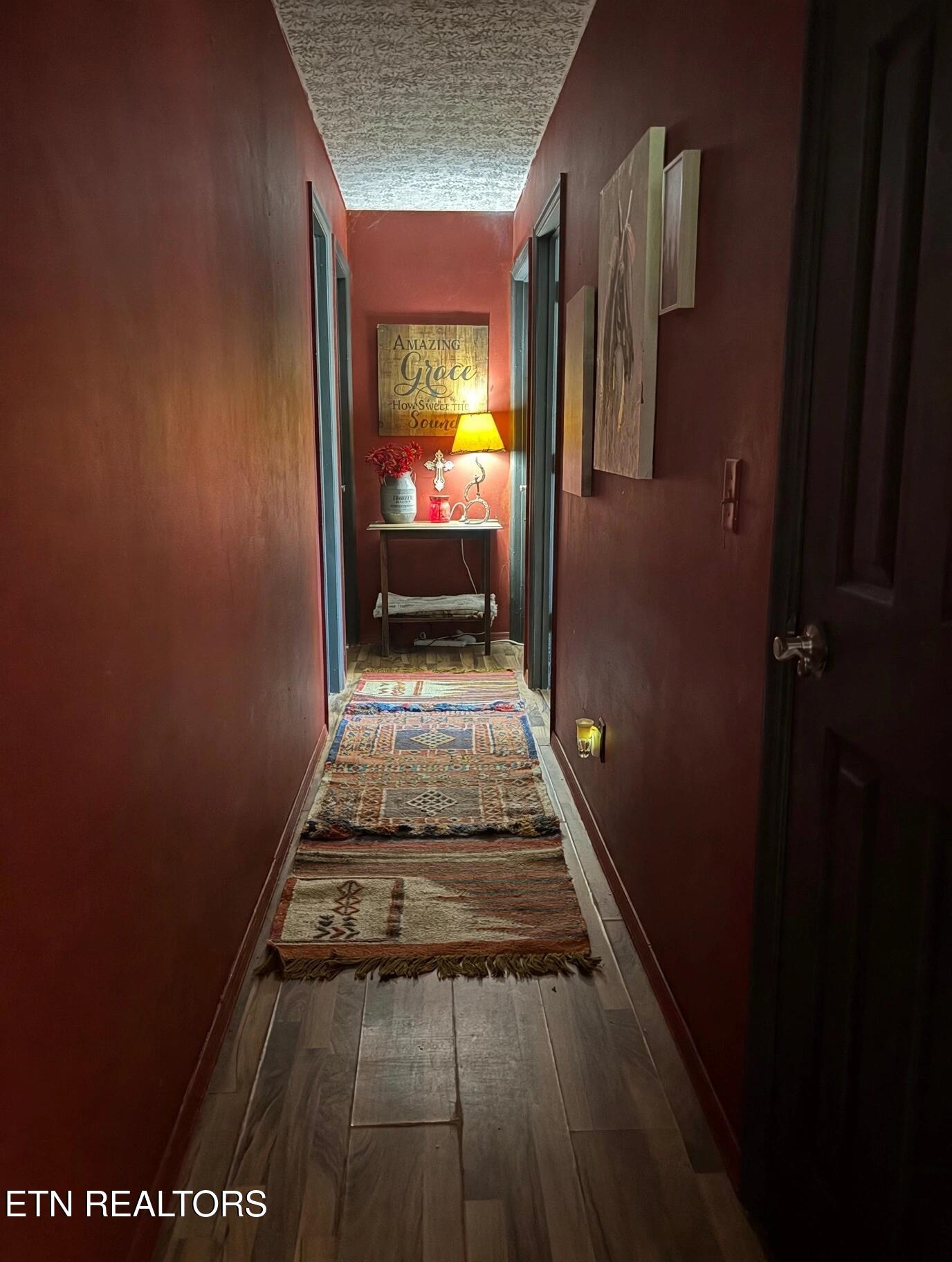 Burgundy hallway lined with patterned rugs, ending at a console table with flowers and a lit lamp.