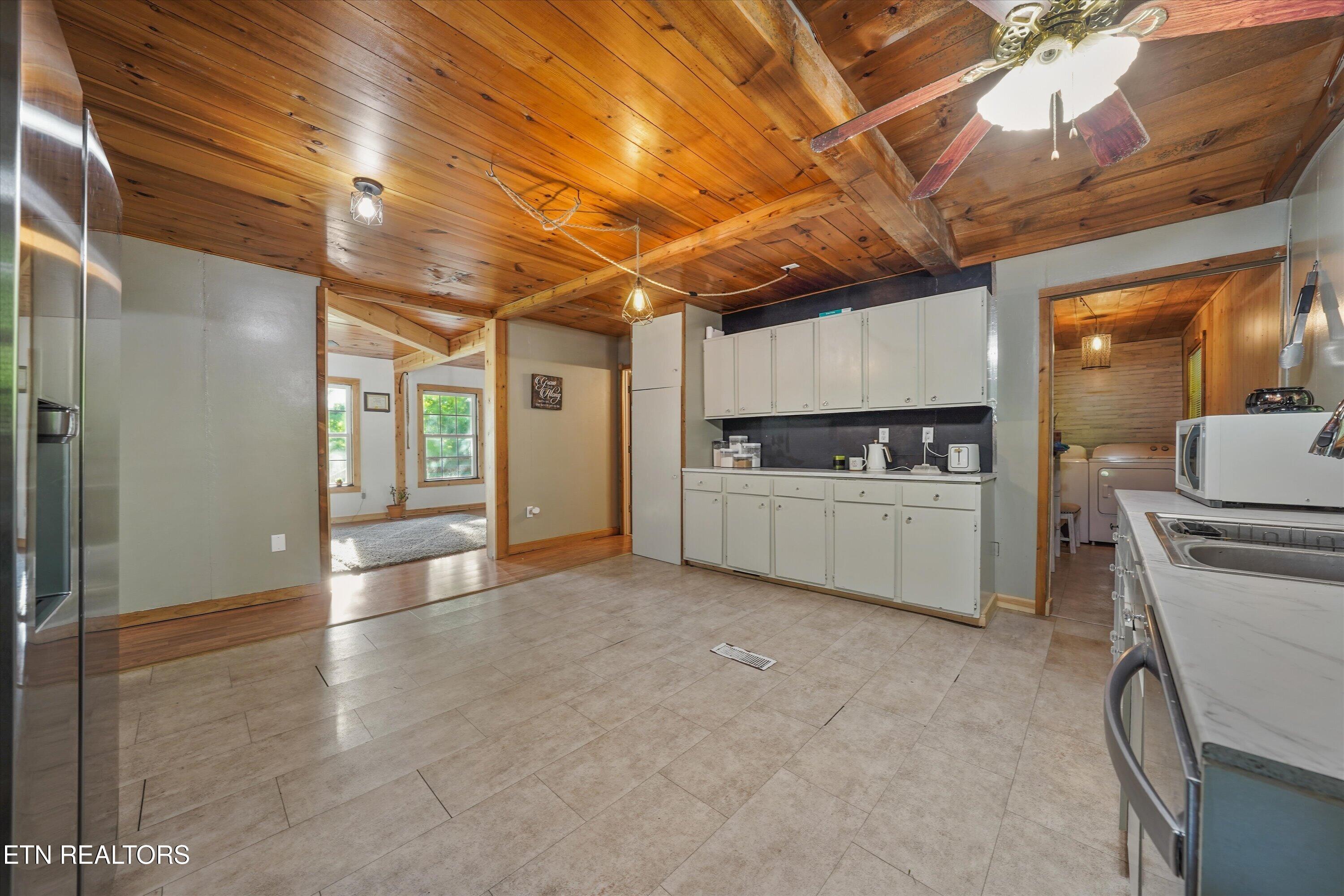 Kitchen with white cabinets and tiled floors beneath a vaulted wood ceiling with exposed beams.