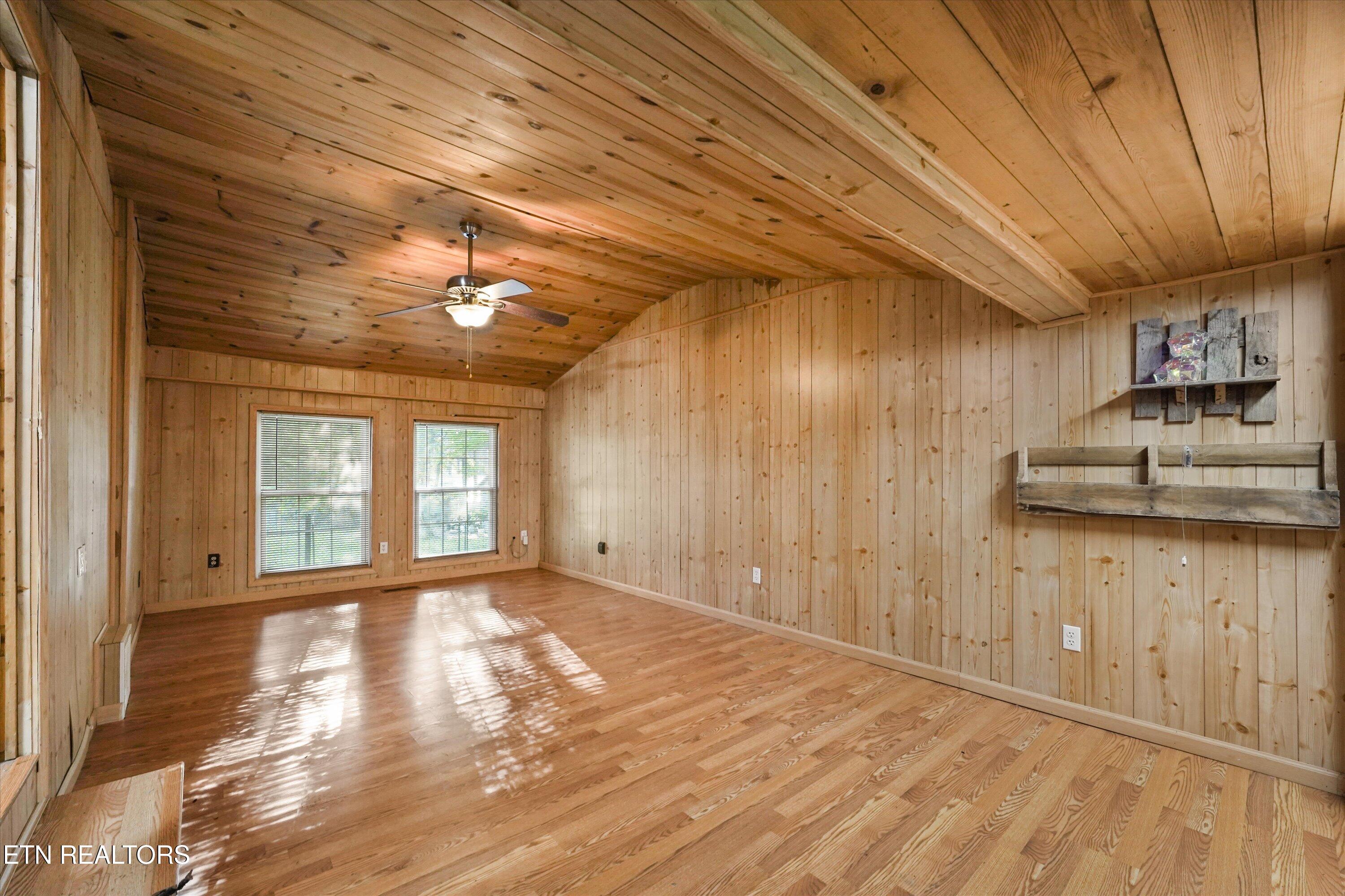 Empty living room with wood-paneled walls, vaulted ceiling, and polished hardwood floors.
