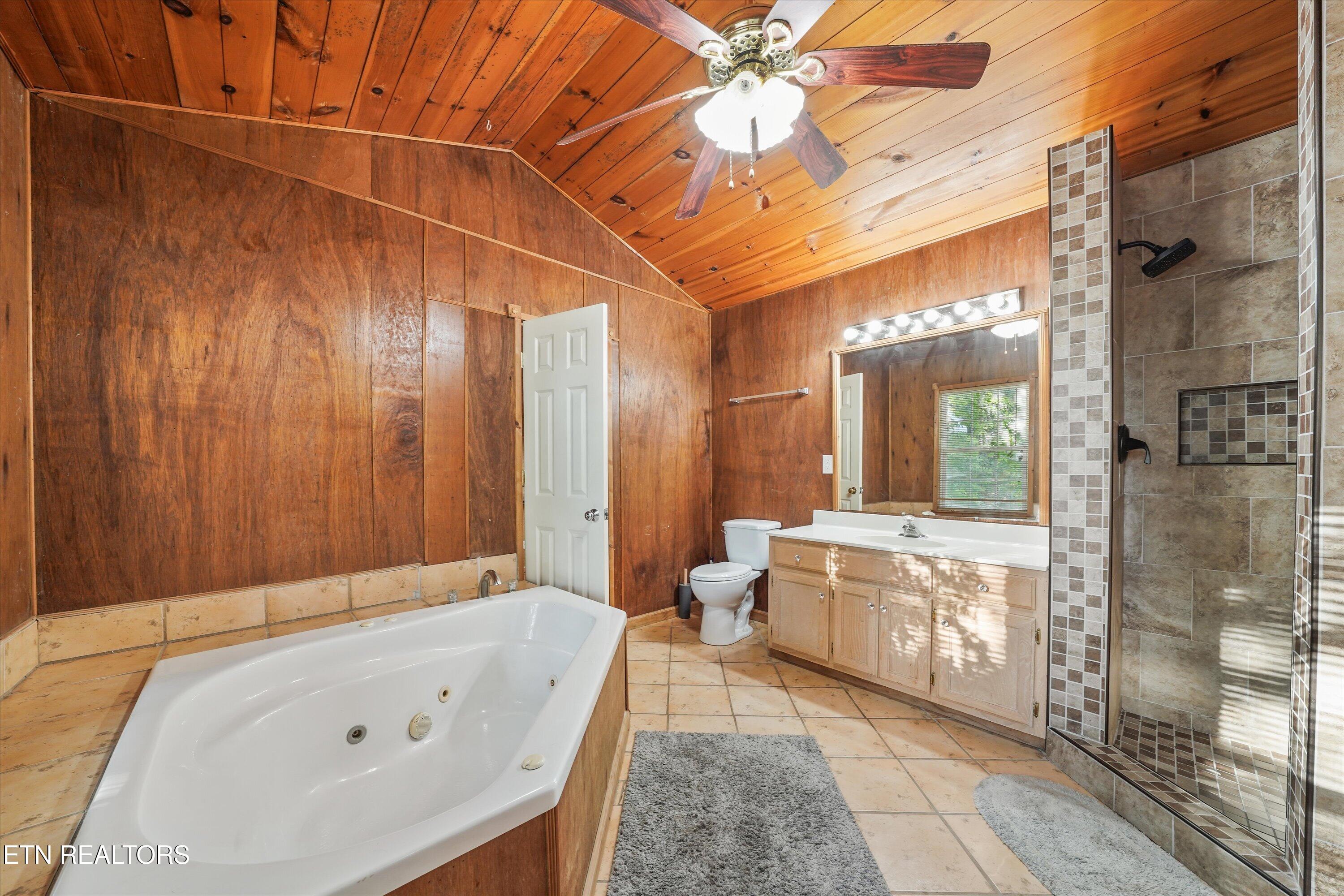 Bathroom with a jetted corner tub, tiled walk-in shower, and vaulted wood-paneled ceiling.
