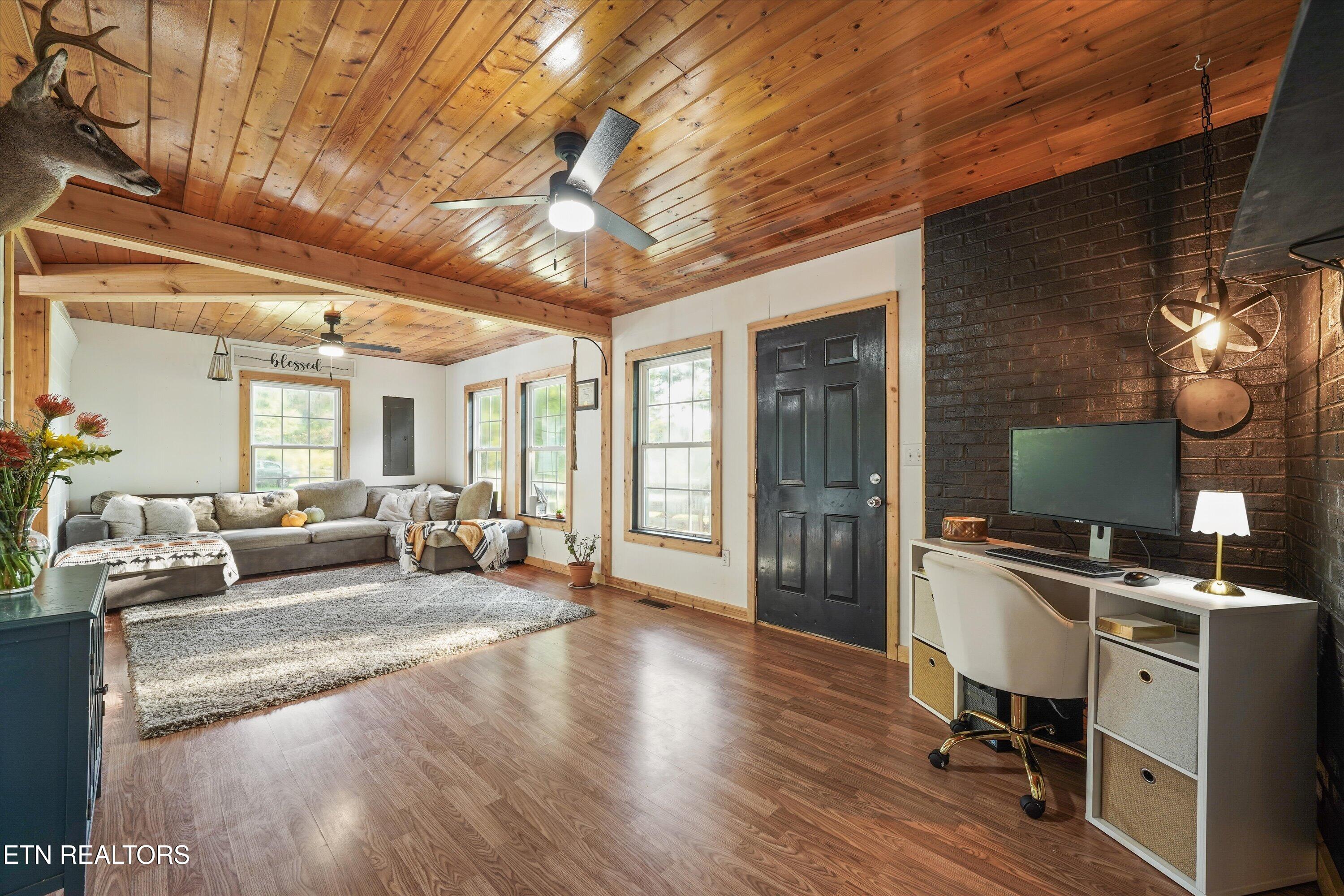 Living room with a pine ceiling, gray sectional, bright windows, and dark brick TV wall.