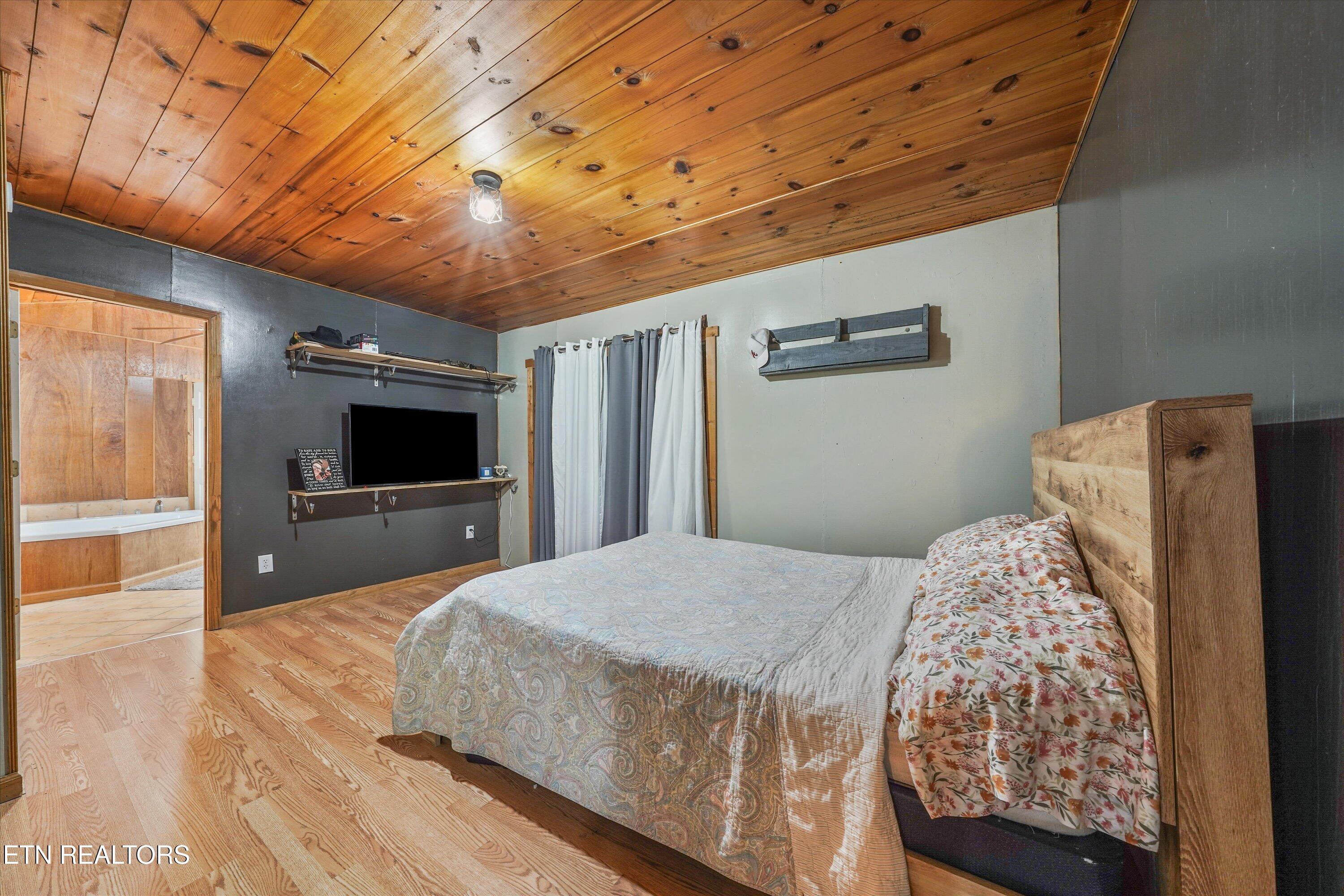 Bedroom with a wood-plank ceiling, hardwood floors, and an open doorway to a bathroom.