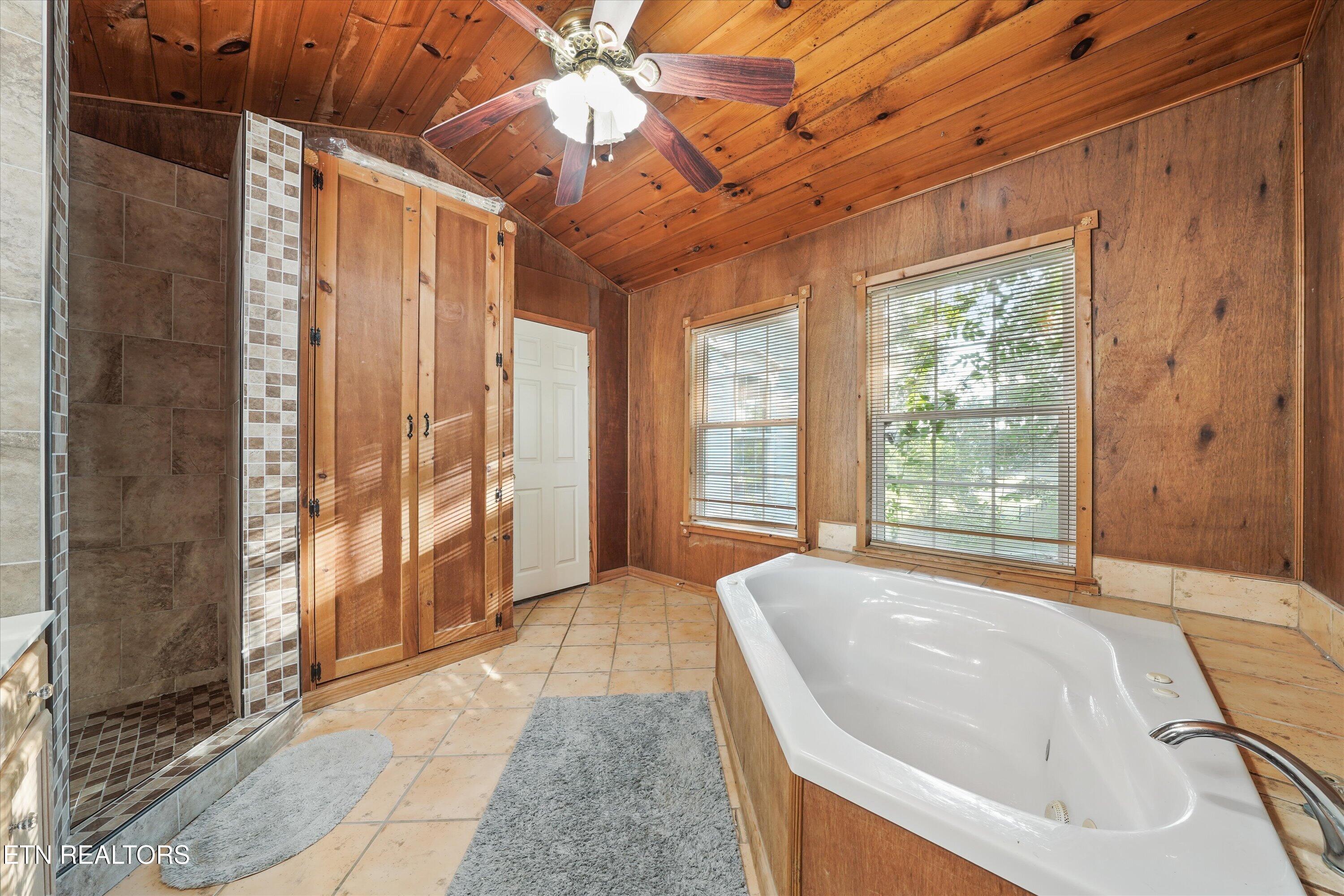 Bathroom with a white soaking tub, tiled walk-in shower, and warm wood-paneled walls and ceiling.