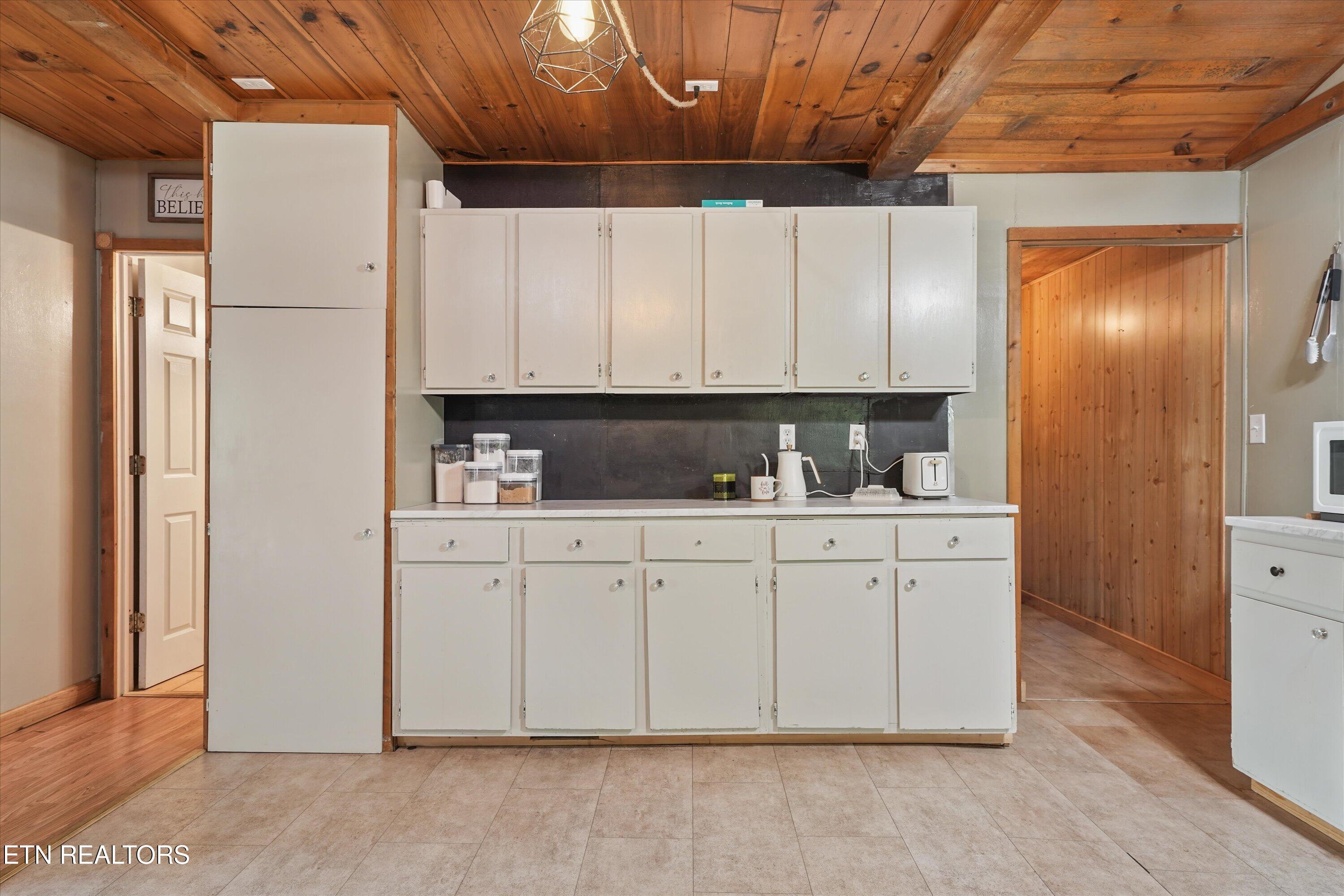 Kitchen with white cabinets, dark backsplash, and a warm wood-plank ceiling.