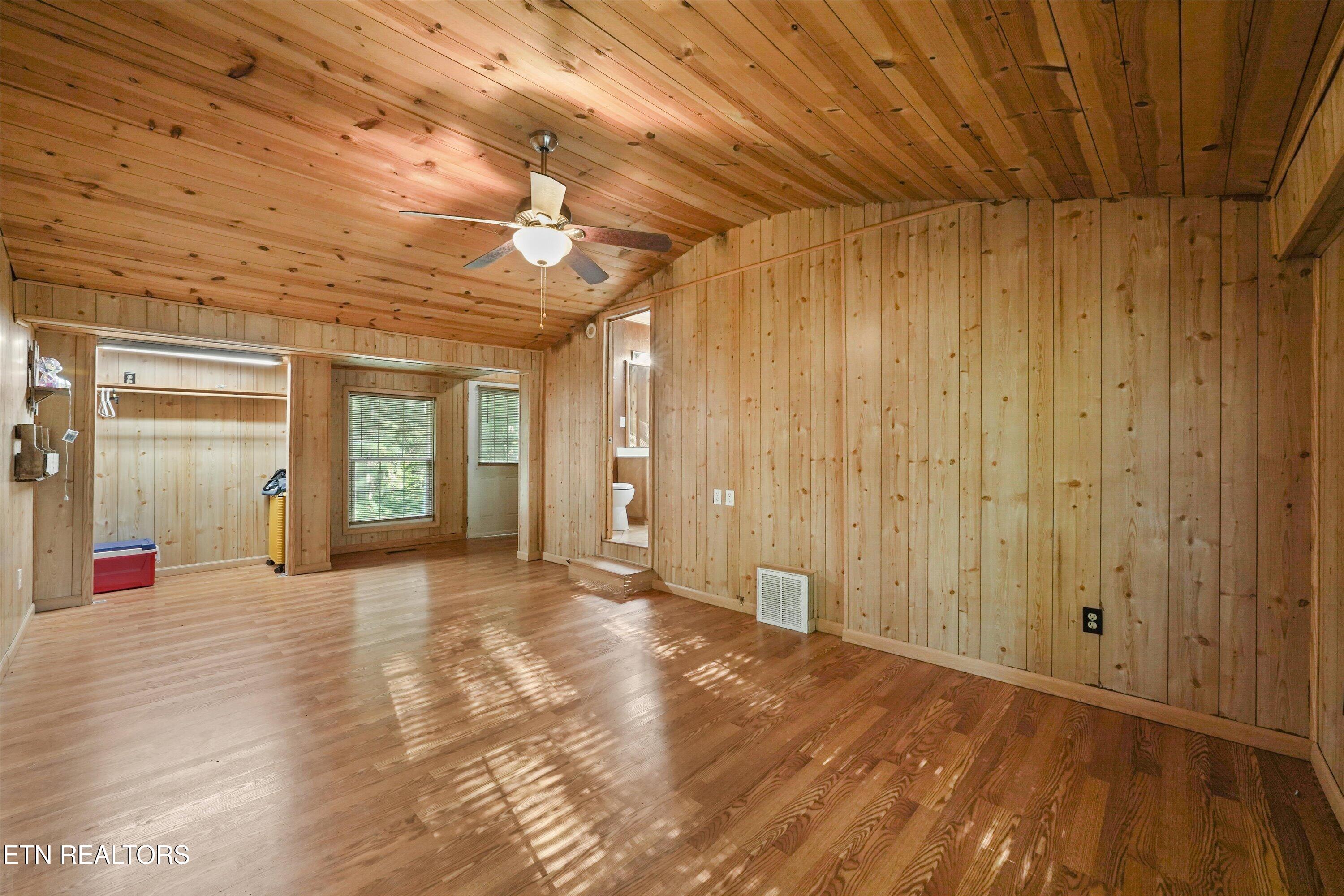 Wood-paneled room with hardwood floors, a plank ceiling, ceiling fan, and open closet area.