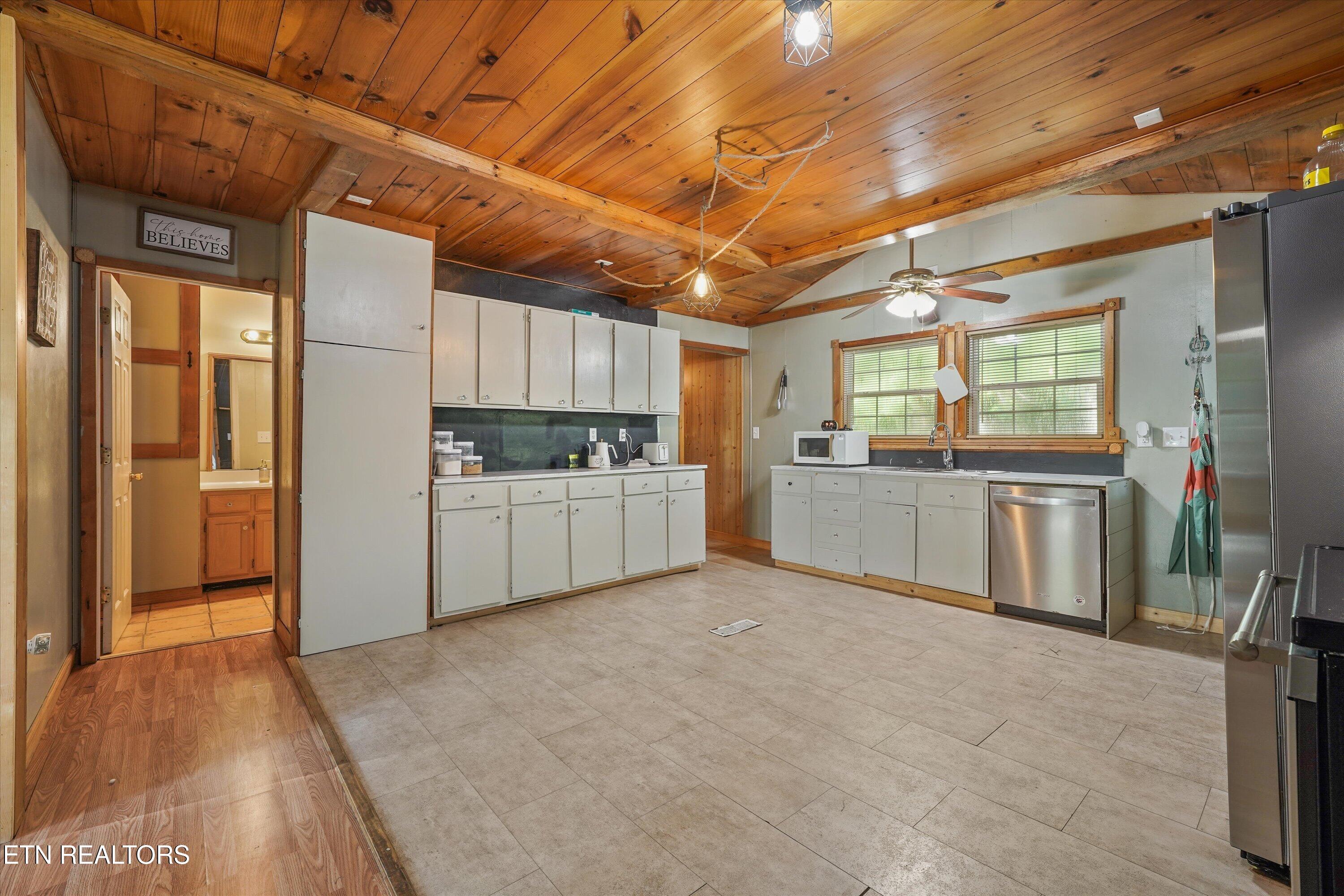 Kitchen with white cabinets, stainless-steel appliances, and a warm wood-plank ceiling with exposed beams.
