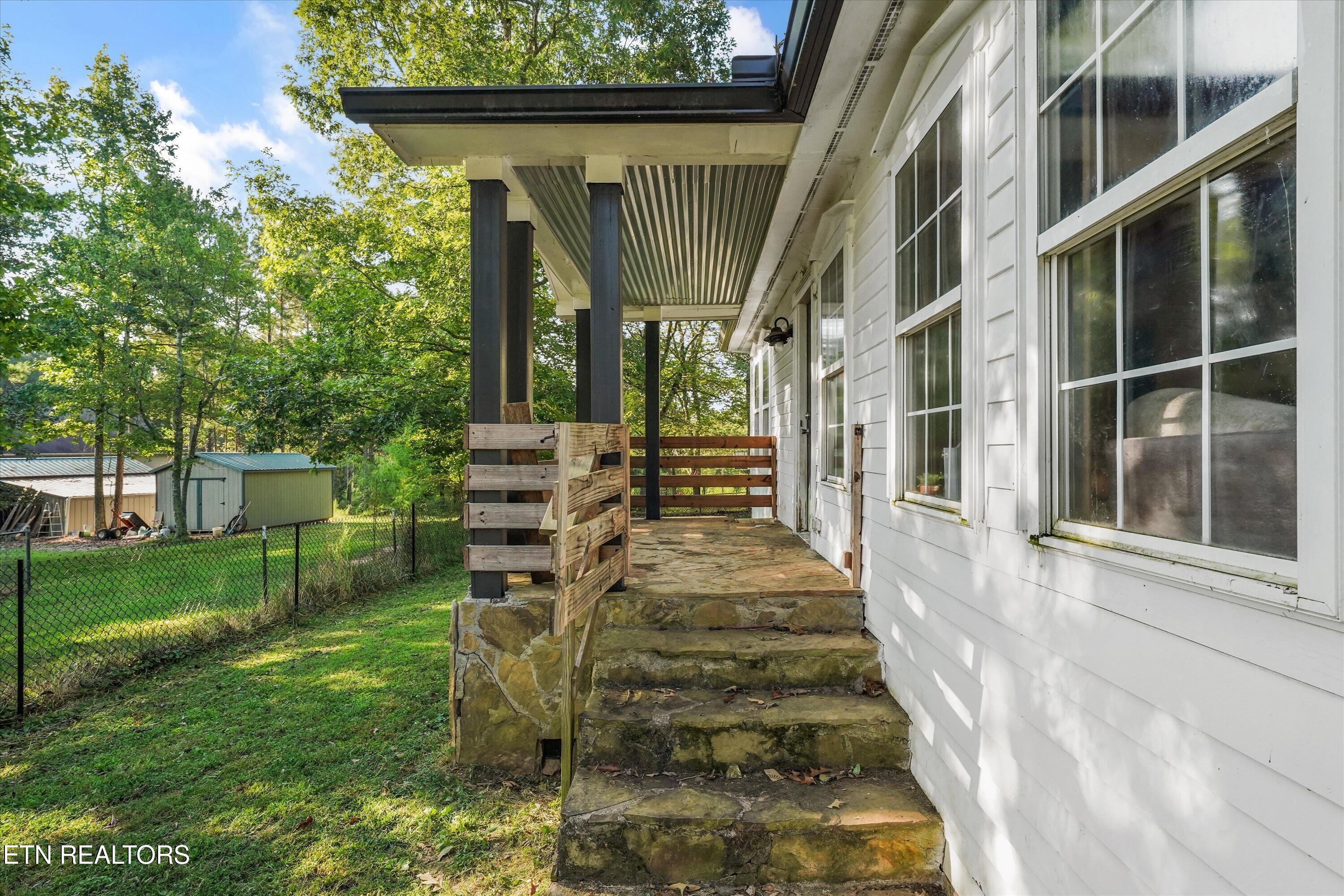 Covered porch with stone steps and wooden railing beside a white-sided house.