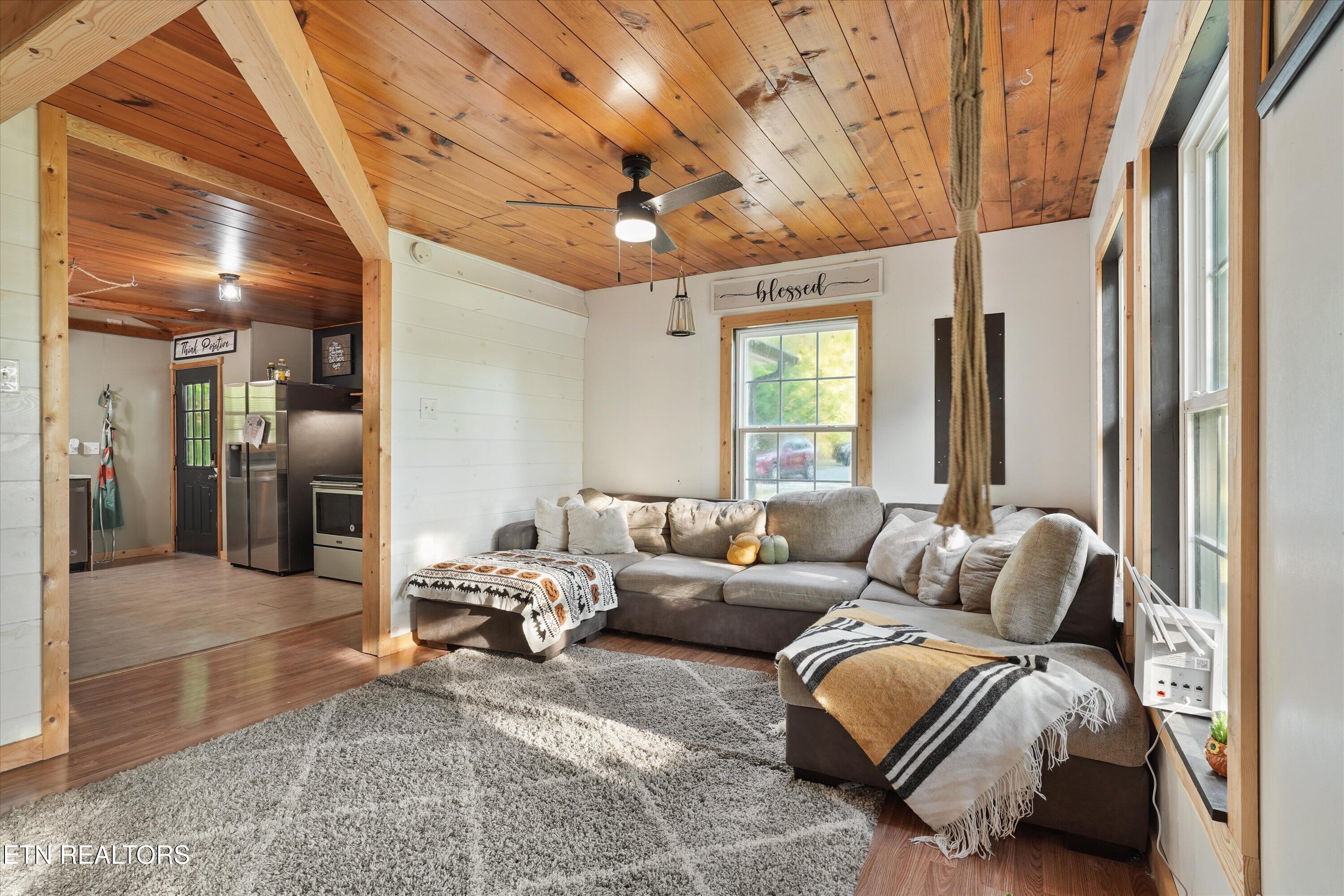 Living room with a gray sectional, shag rug, and warm wood-plank ceiling beside an open kitchen.