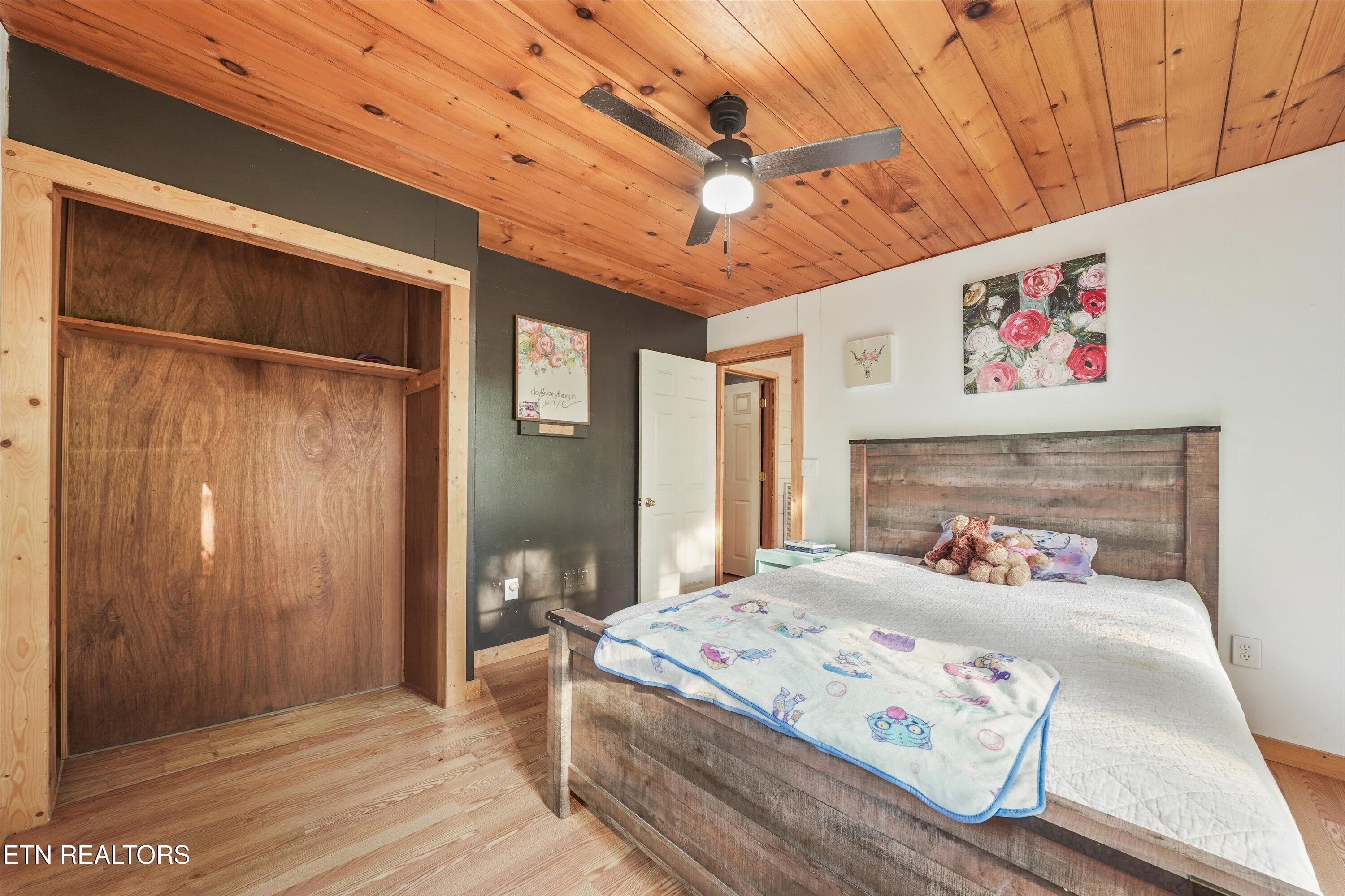 Bedroom with a rustic wood bed, built-in shelving nook, and warm wood-plank ceiling.