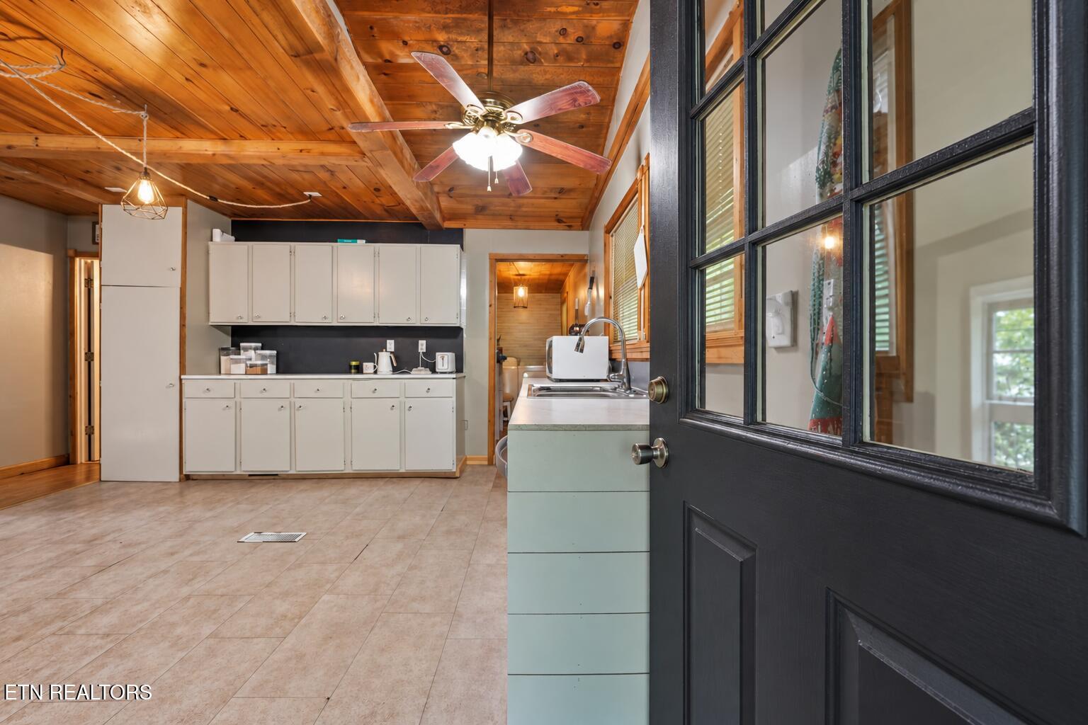 Kitchen with white cabinets, a wood-plank ceiling, and an open black glass-paneled door.