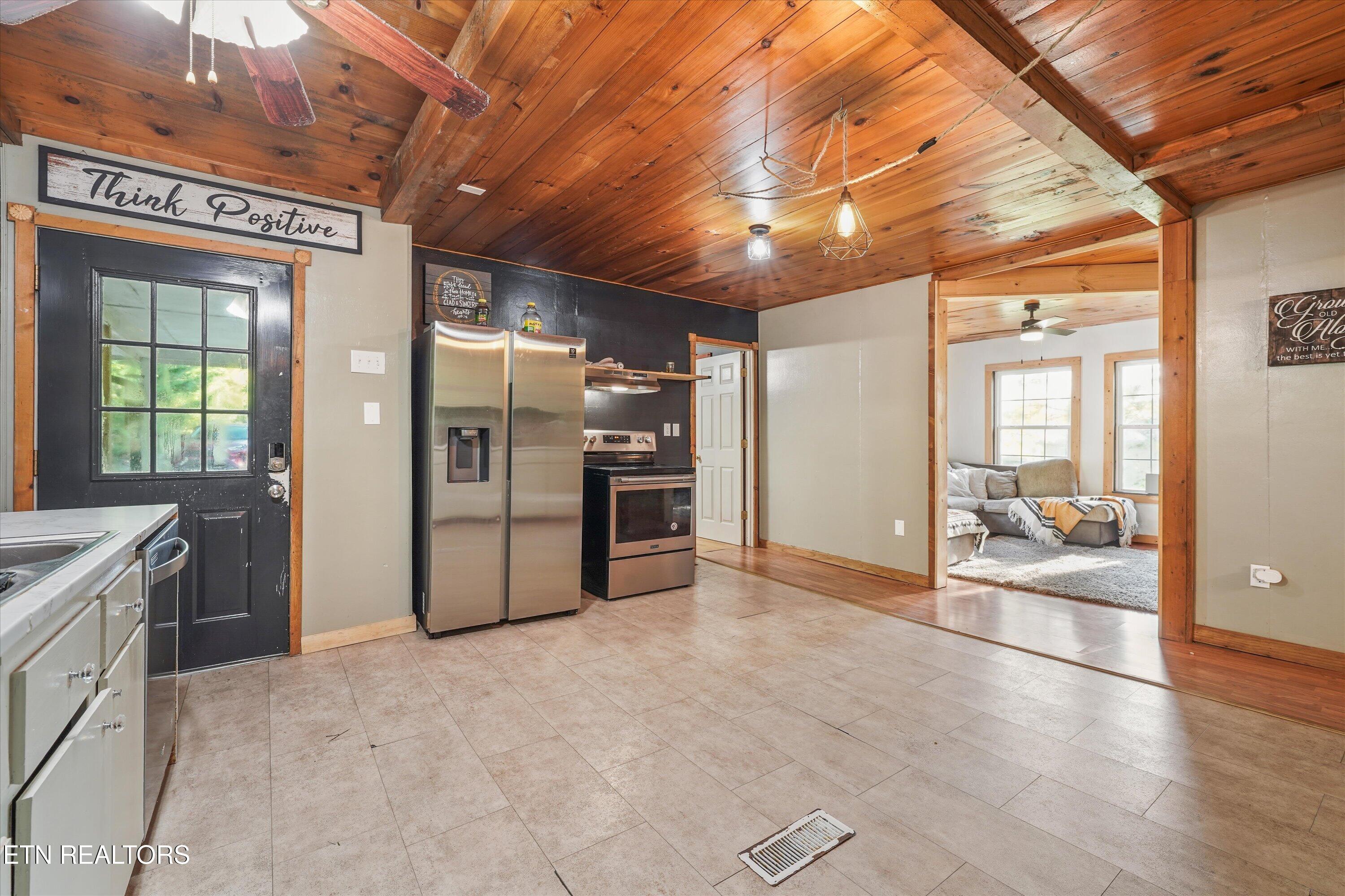 Kitchen with stainless steel appliances and a wood-plank ceiling, opening into a furnished living room.