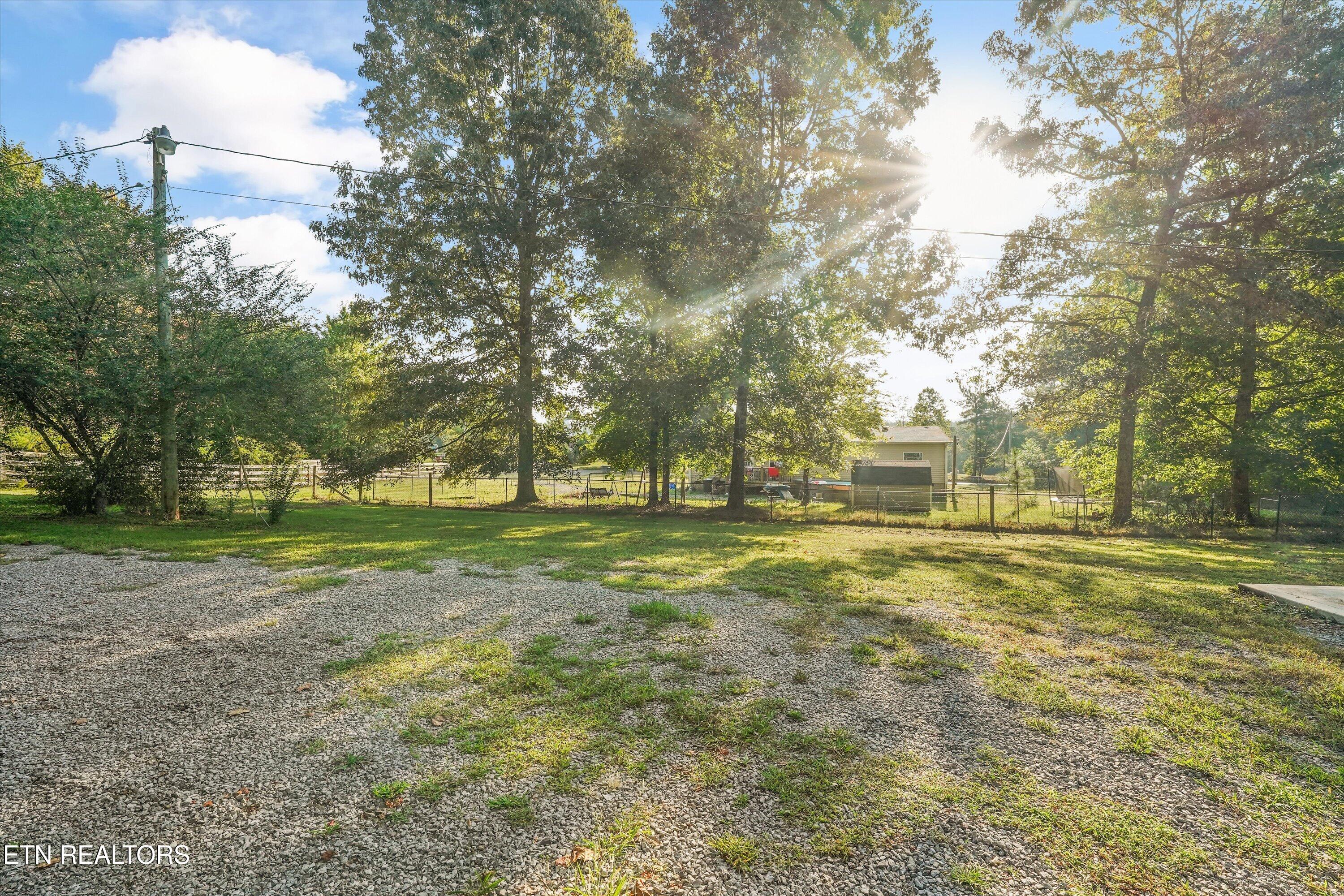 Gravel driveway and tree-shaded yard with a fenced area and small outbuilding.