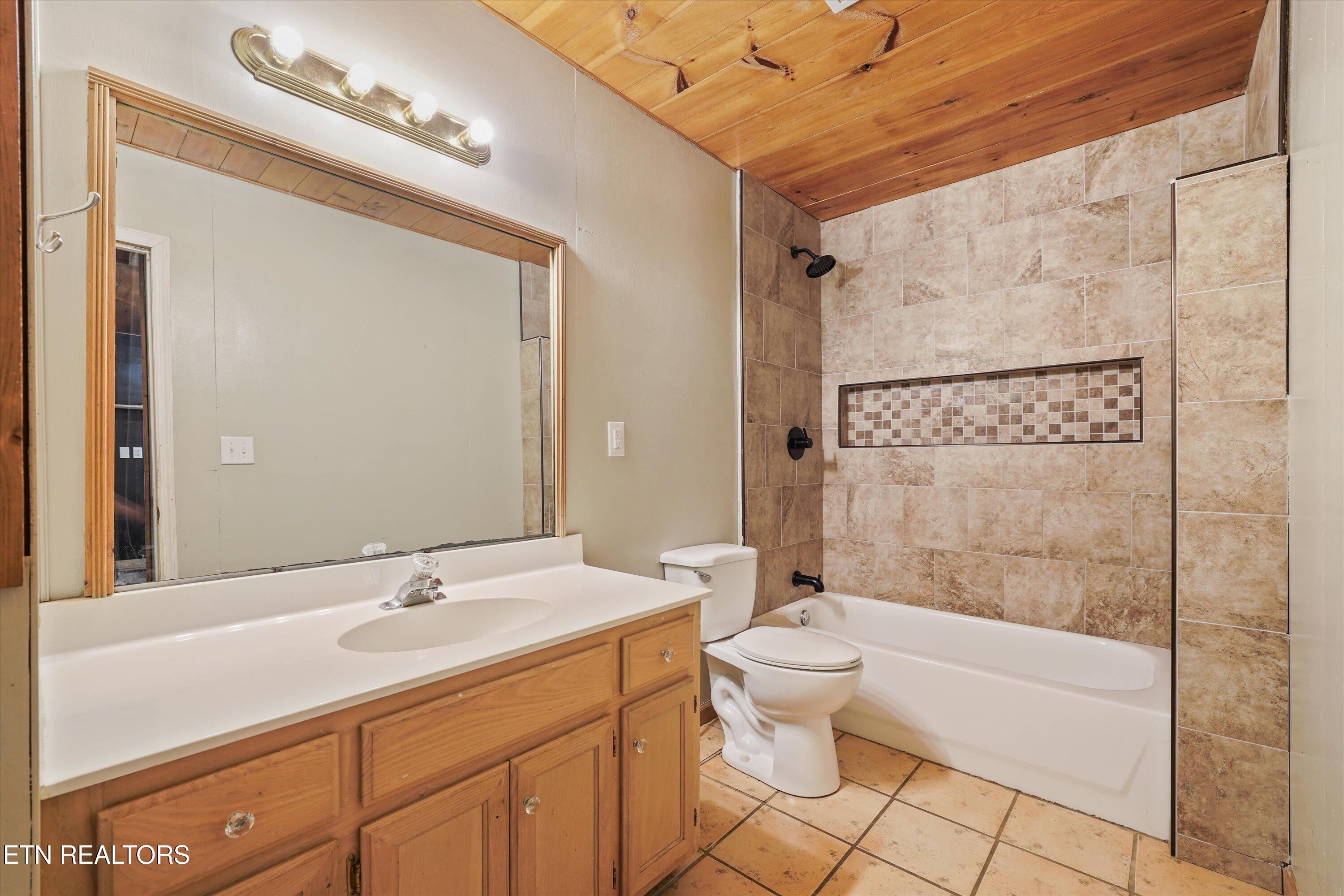 Bathroom with a wood vanity and mirror beside a tan-tiled tub and shower.