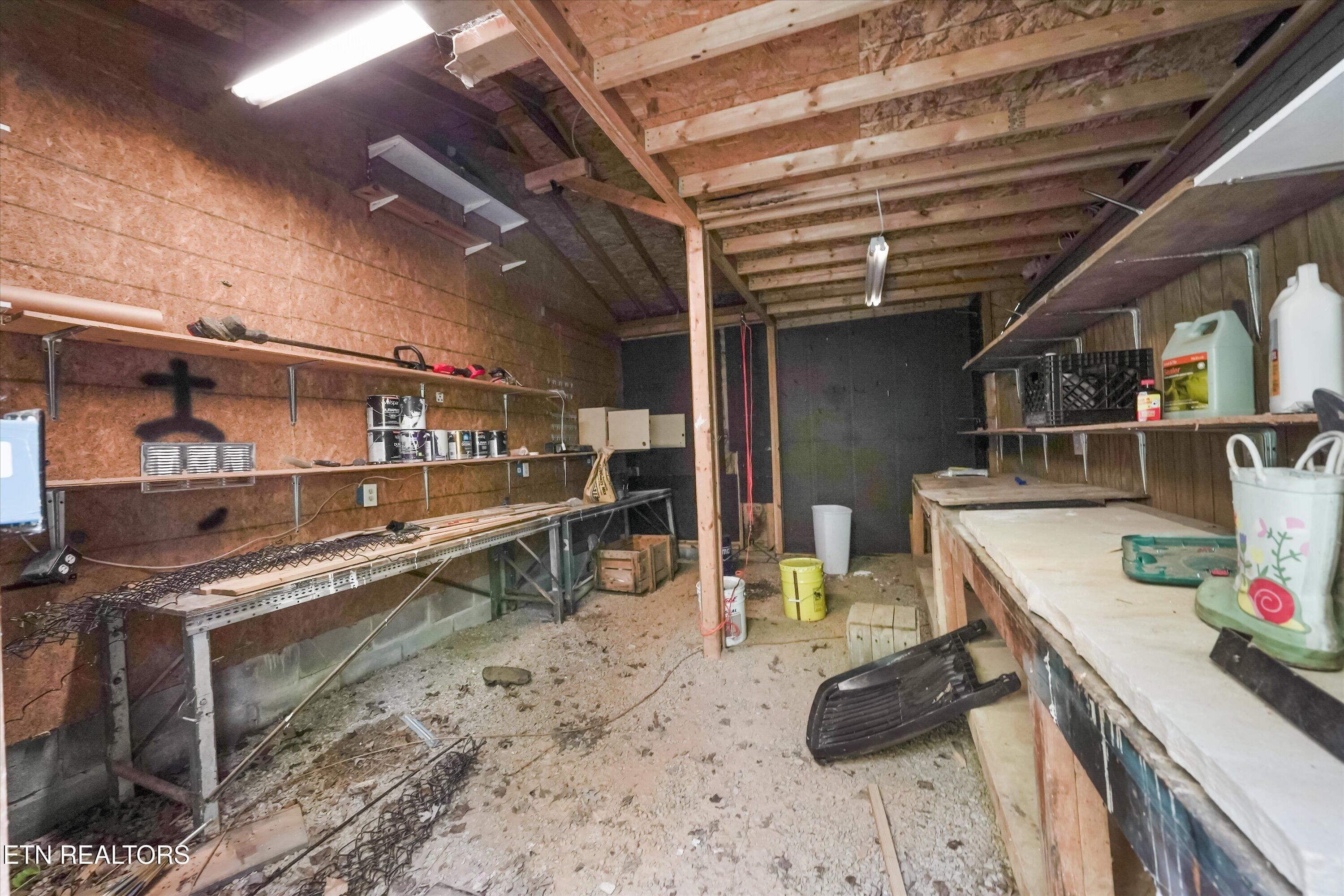 Workshop with exposed wood framing, long workbenches, wall shelves, and supplies.