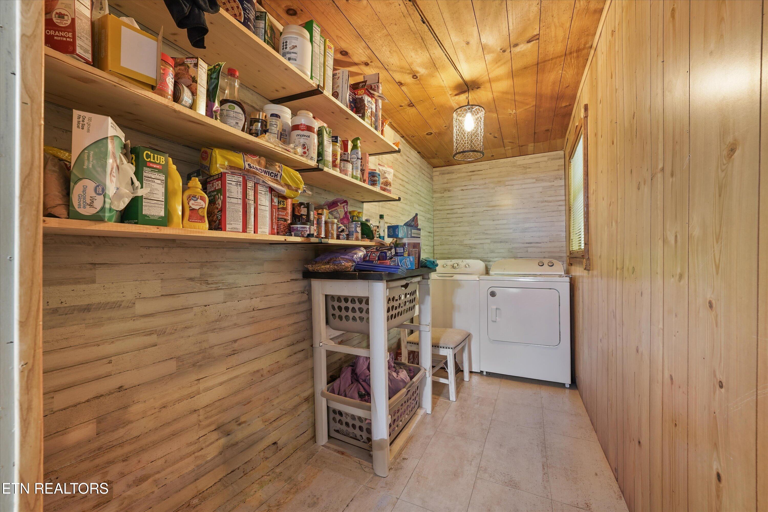 Laundry room with a washer and dryer, stocked open shelves, and wood-paneled walls.