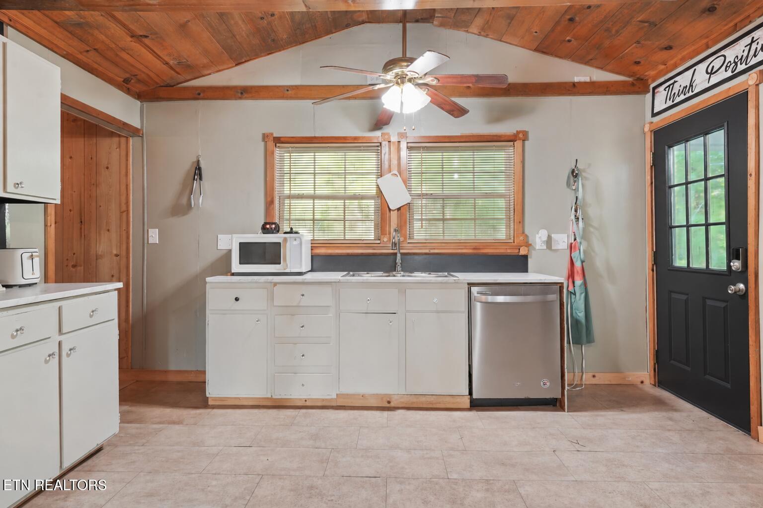 Kitchen with white cabinets, stainless-steel dishwasher, and vaulted wood ceiling with exposed beams.