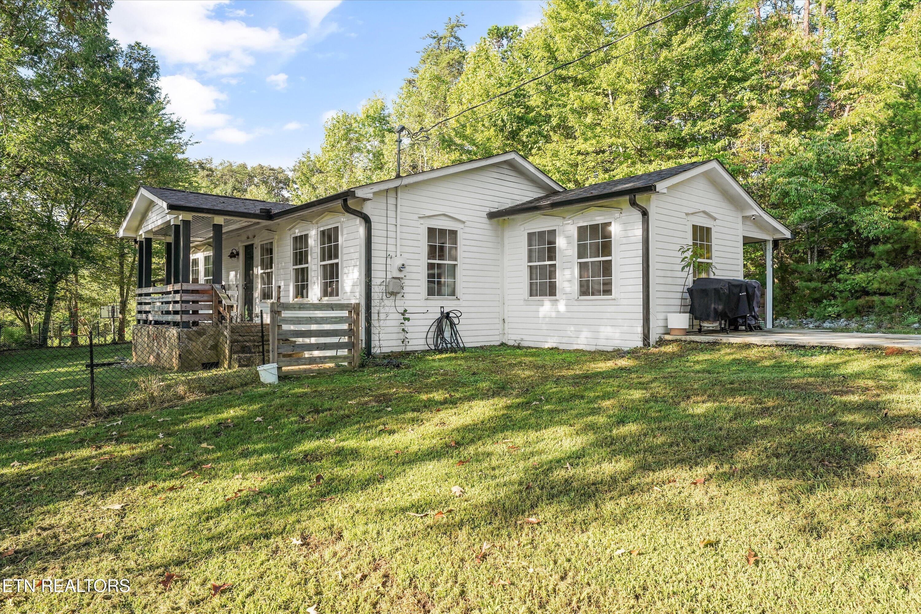 White single-story house with a covered deck and fenced, tree-lined lawn.